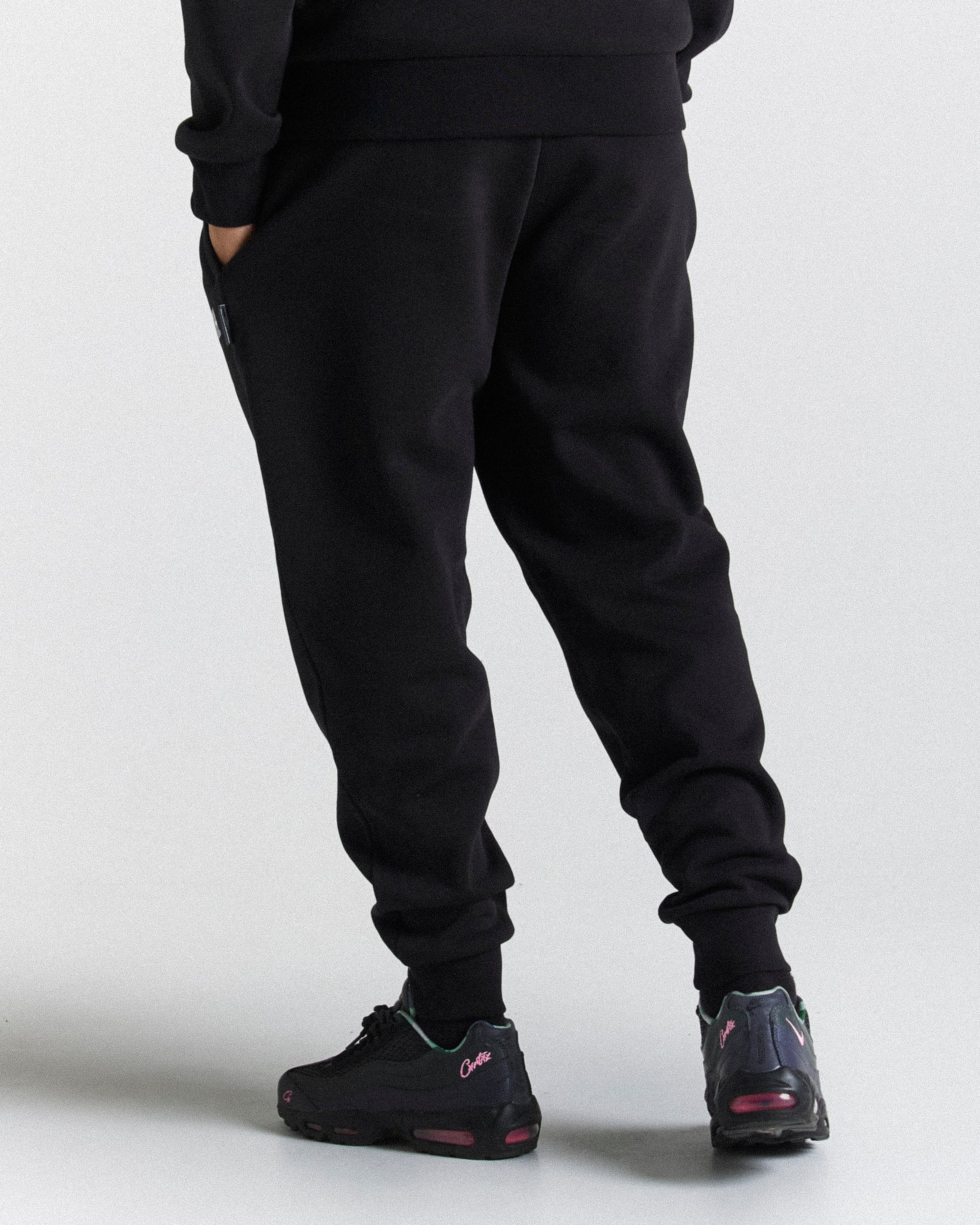 Black jogger sweatpants worn by a model, shown from the back and side against a light gray studio background. The model is also wearing black sneakers.