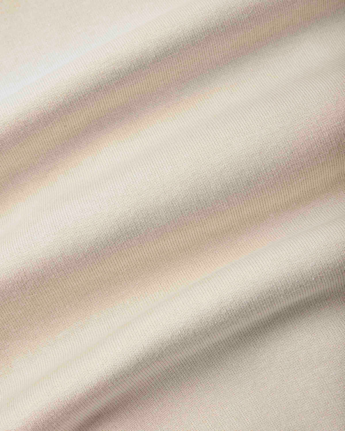 A close-up of draped fabric with a soft, warm off-white or cream tone and subtle pinkish-beige shading from the folds.