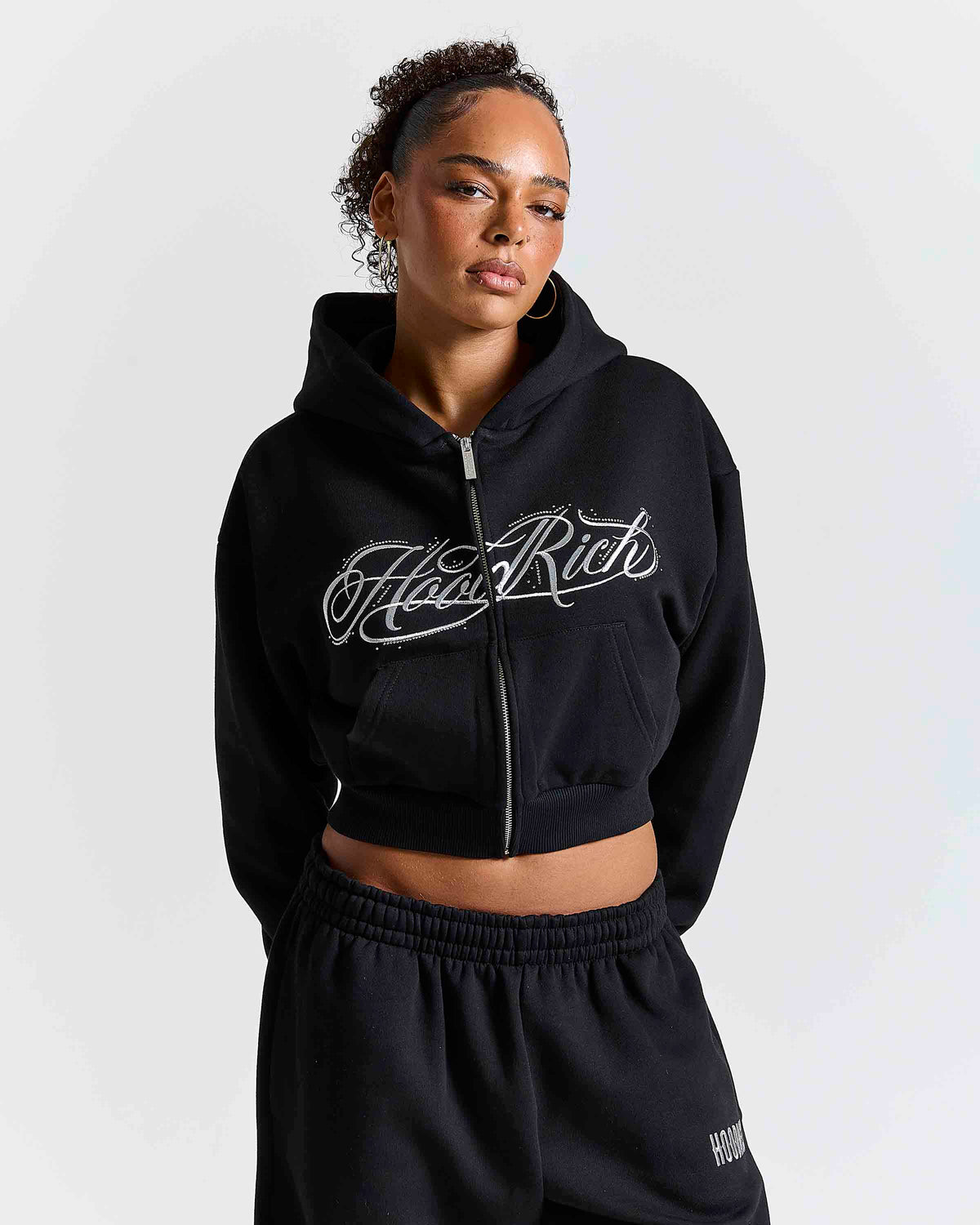 Displays a model wearing the Black 'Hoodrich' branded women's Solace Full Tracksuit