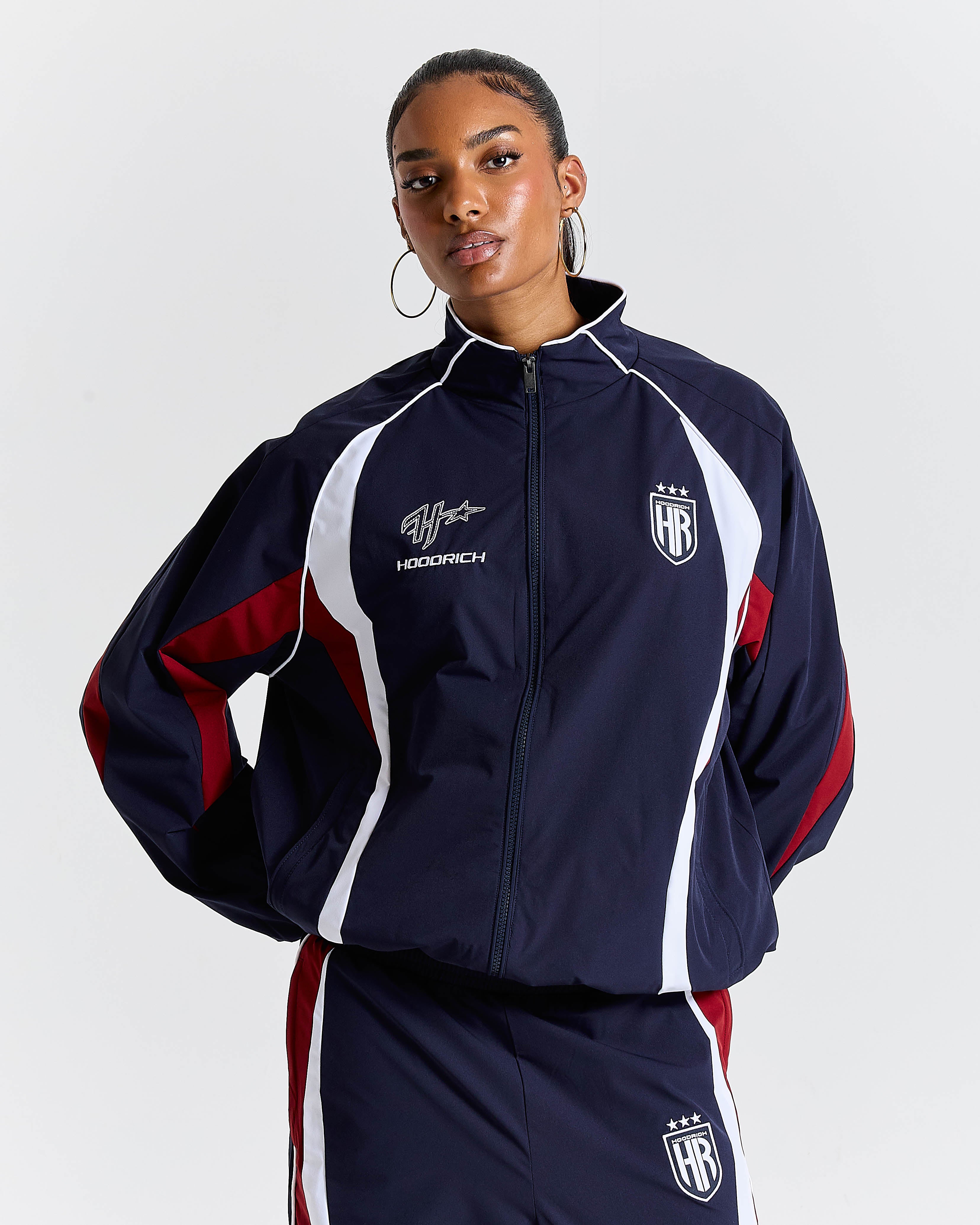 Person wearing a navy tracksuit with red and white accents on a light gray background