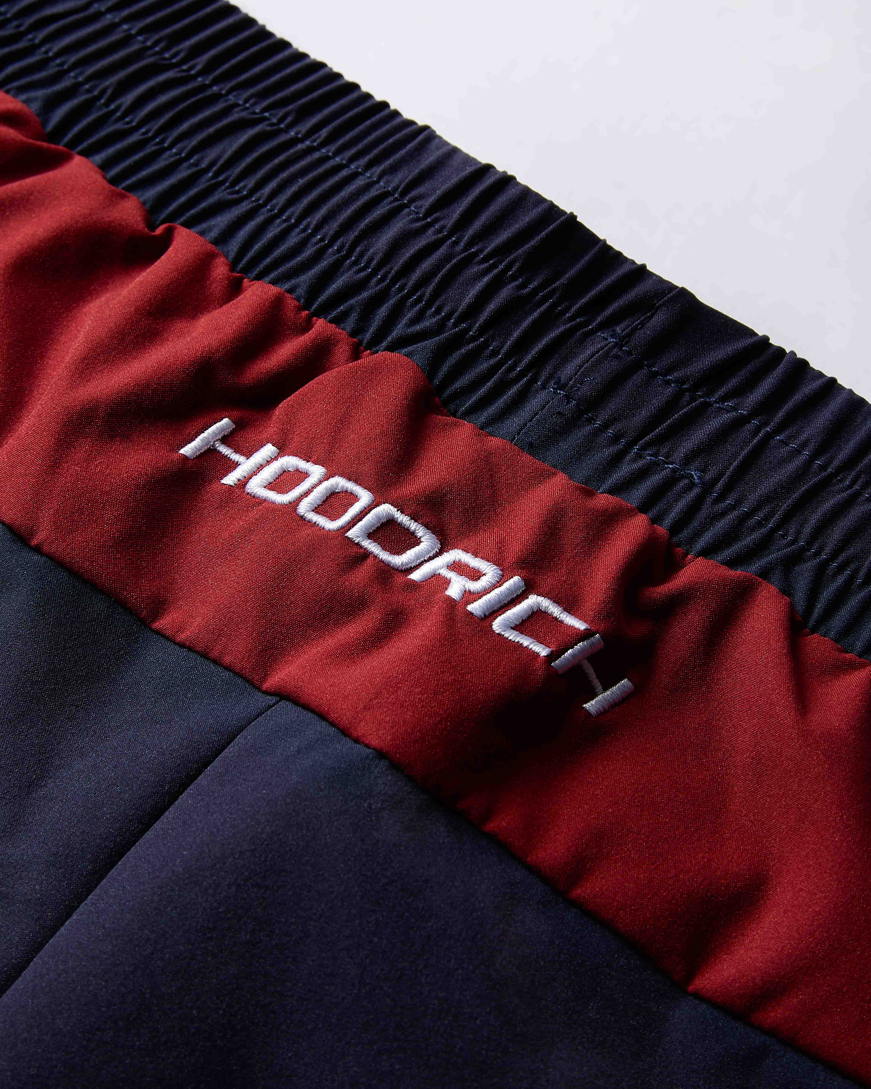 Close-up of a red and navy jacket with 'Hoodrich' branding on a white background