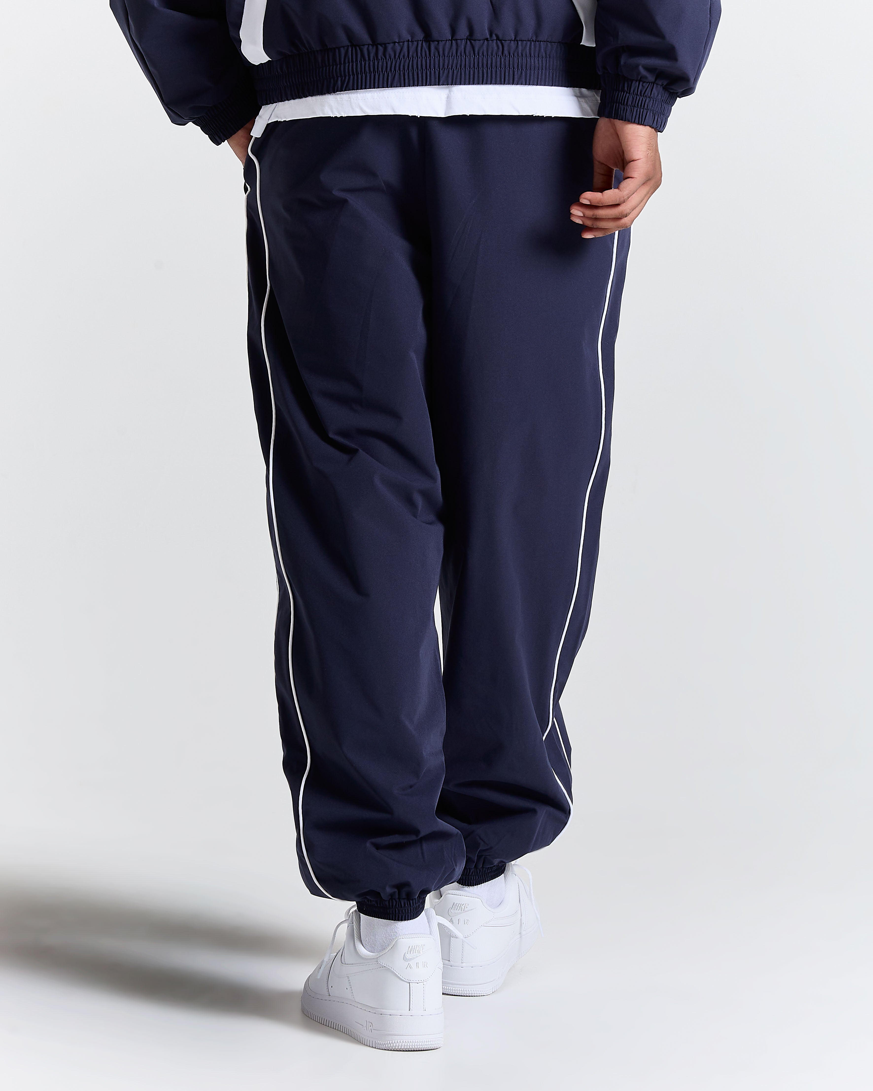 Navy tracksuit with white stripes worn by a person on a light gray background