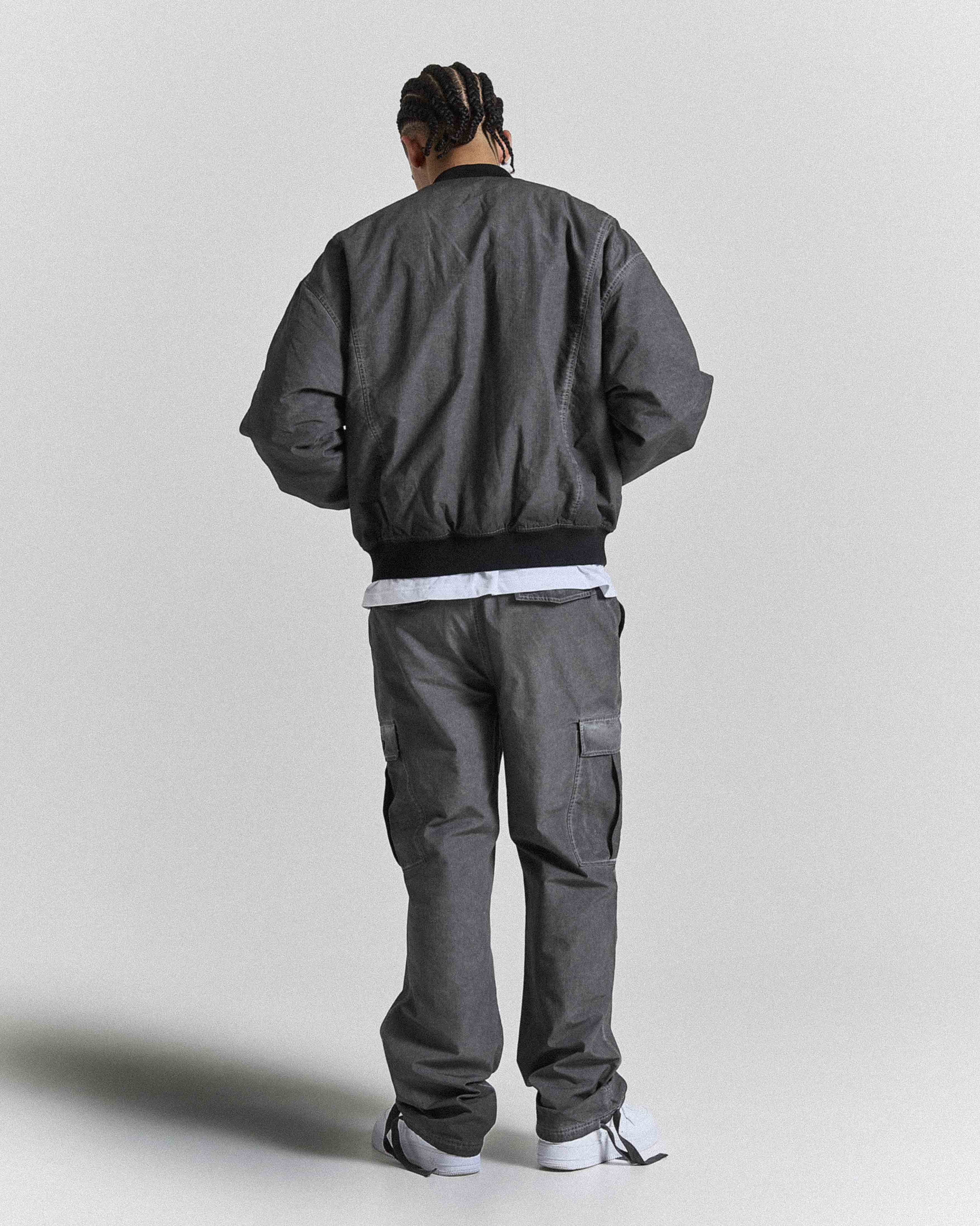 Back view of a male model wearing a gray bomber jacket and pants on a plain background