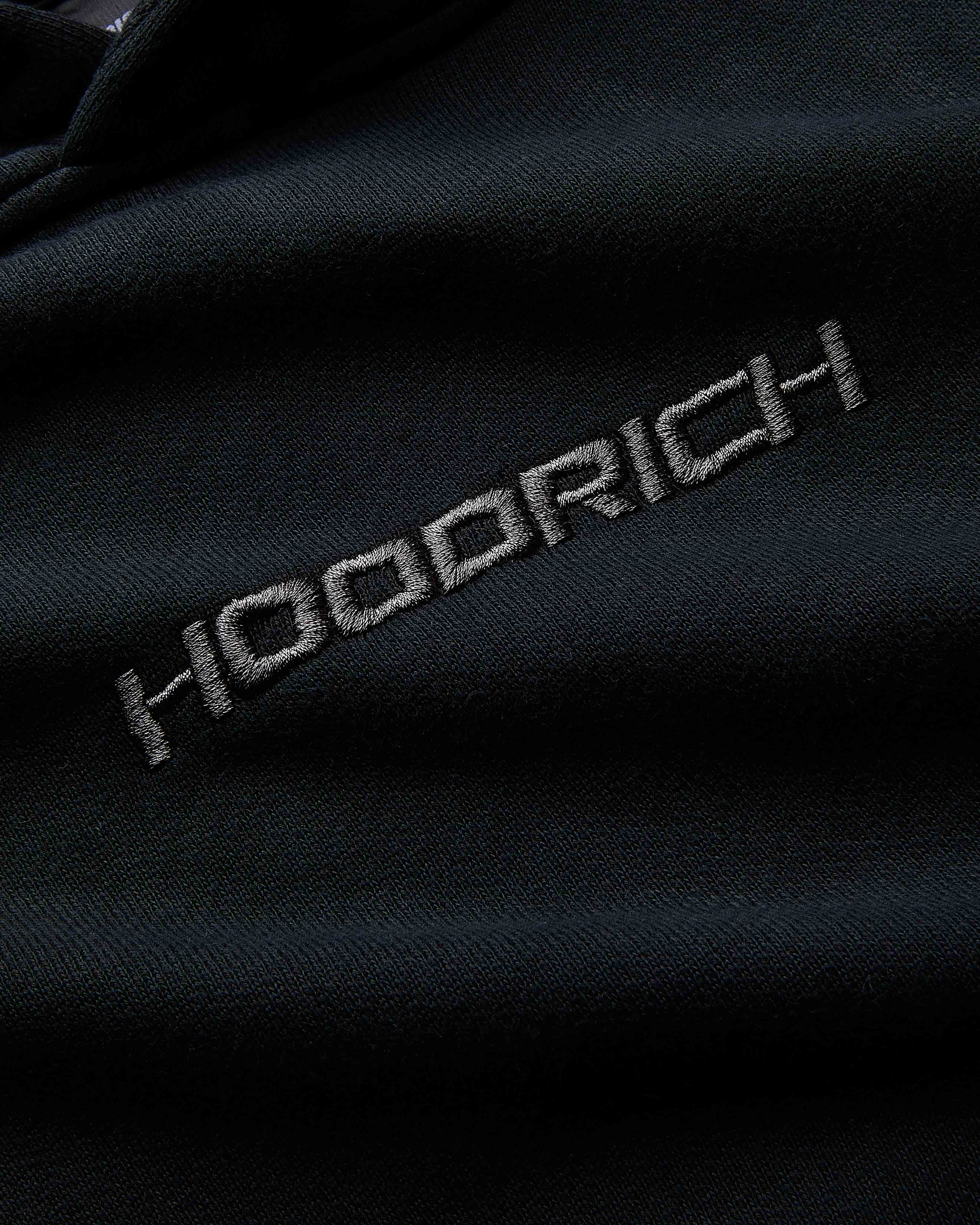 Close-up of a dark fabric with 'Hoodrich' embroidered on it.