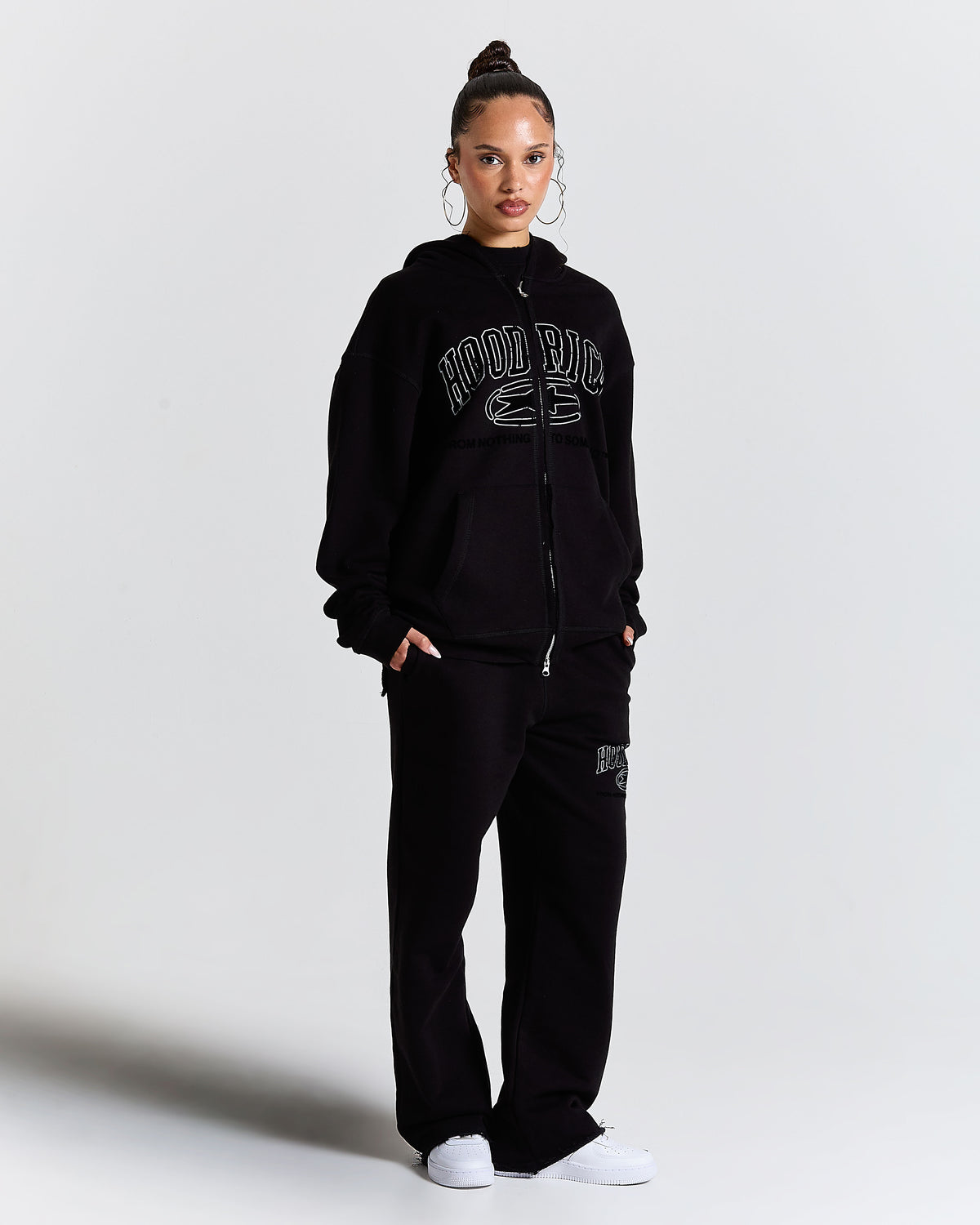 Person wearing a black tracksuit with 'Hood Rich' branding on a light gray background