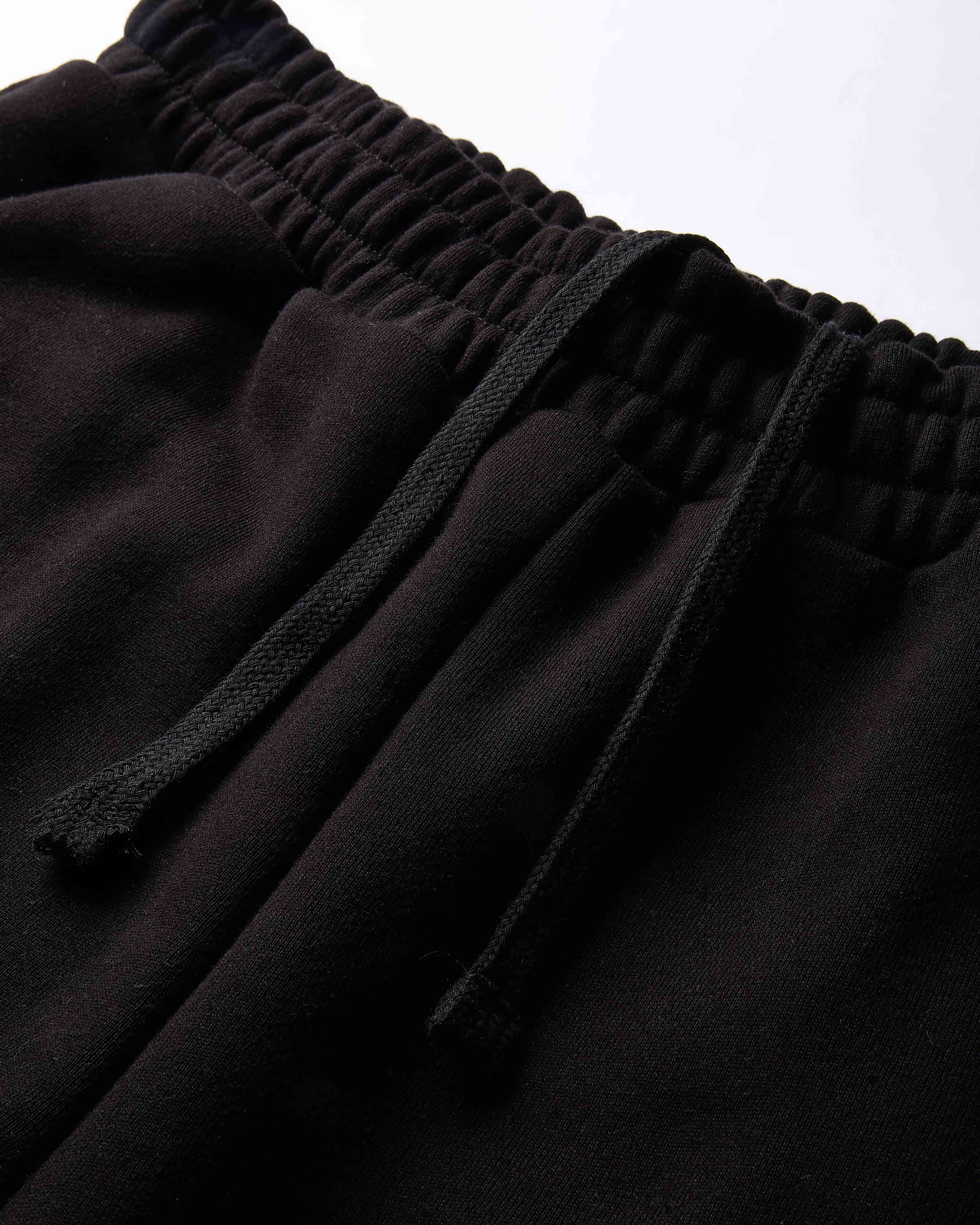 Close-up of black pants with a drawstring waistband on a light gray background