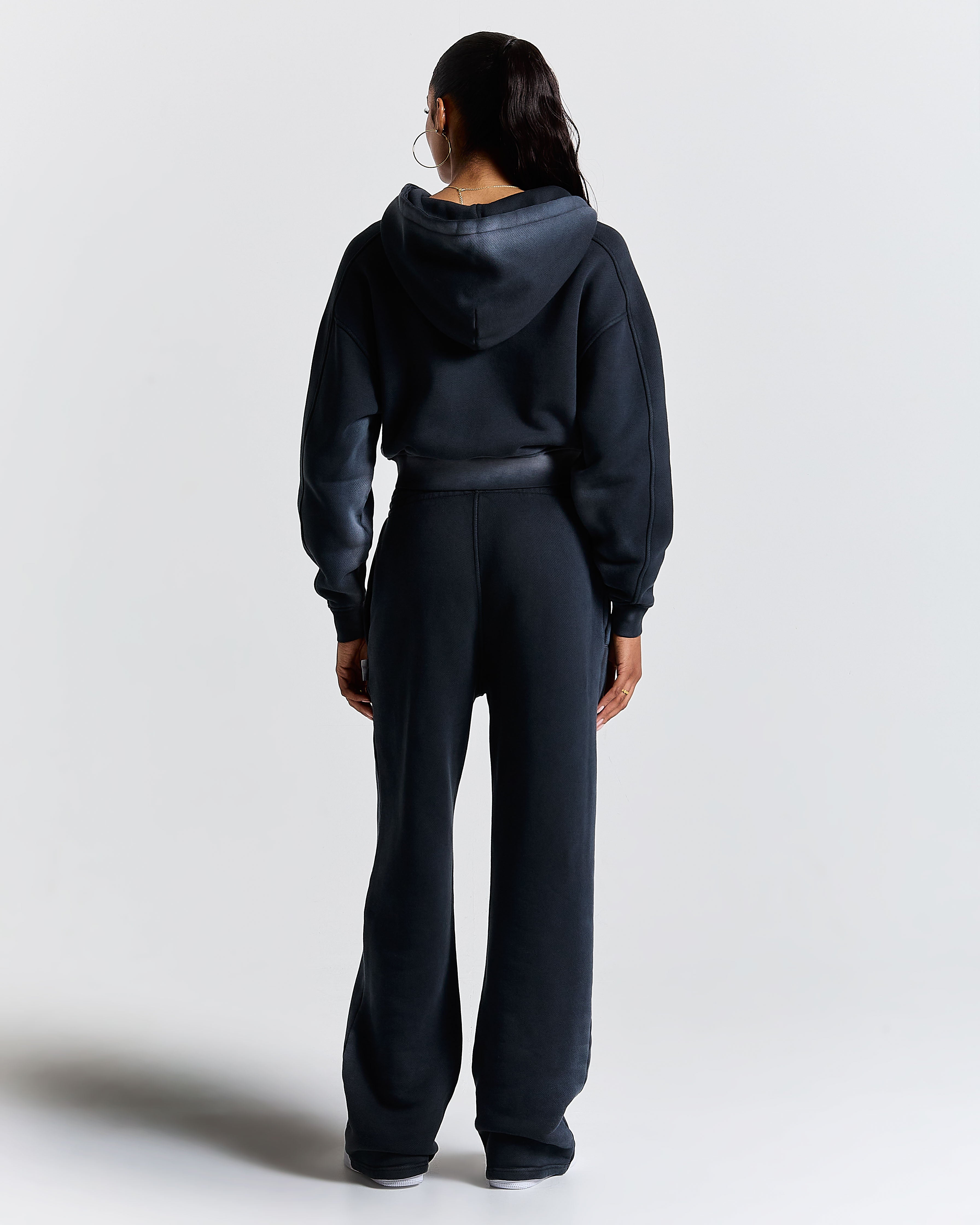 Full-length shot of a female model wearing black wide-leg joggers with an embroidered Hoodrich logo on the leg.