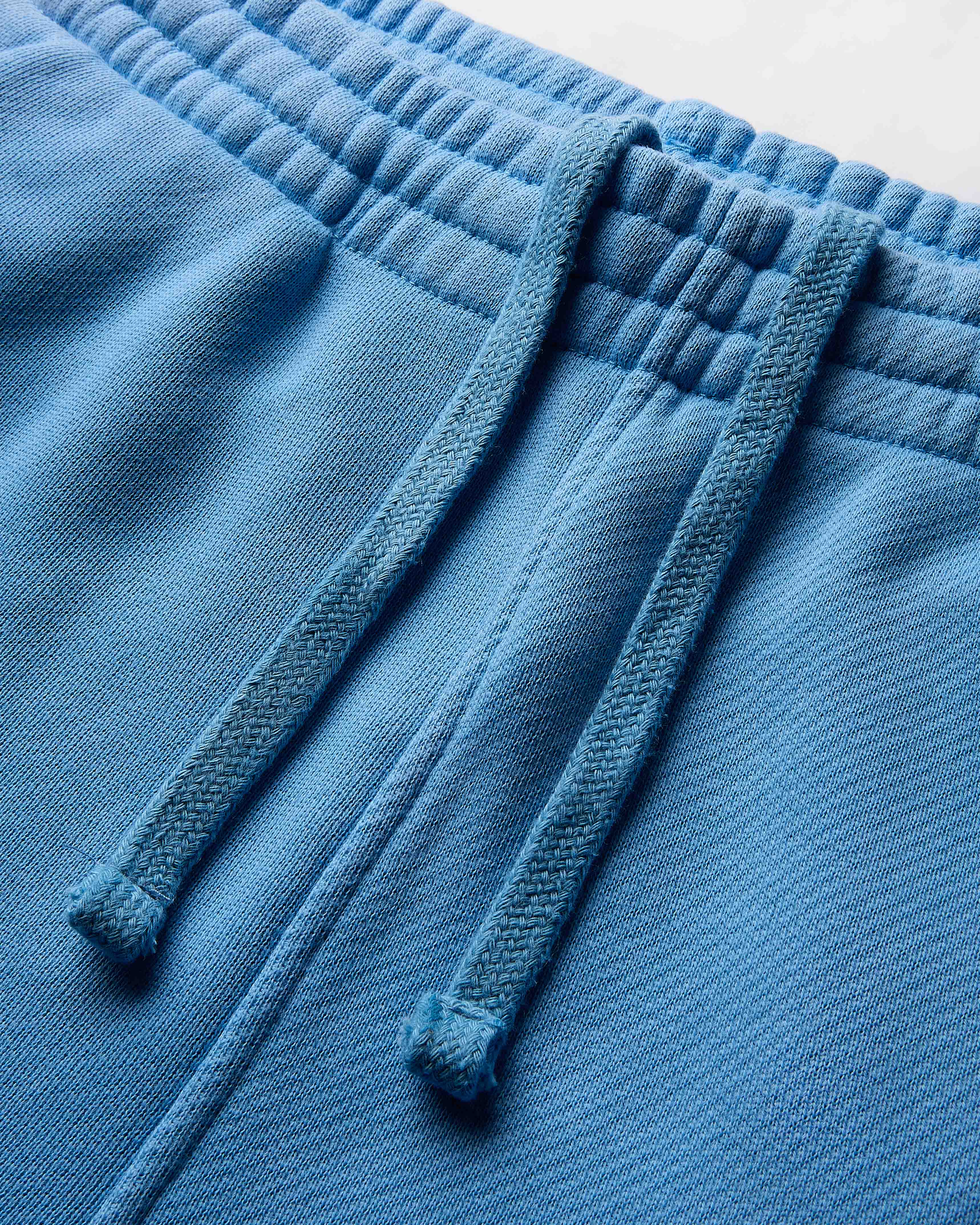Close-up of blue fleece pants with drawstrings on a light gray background
