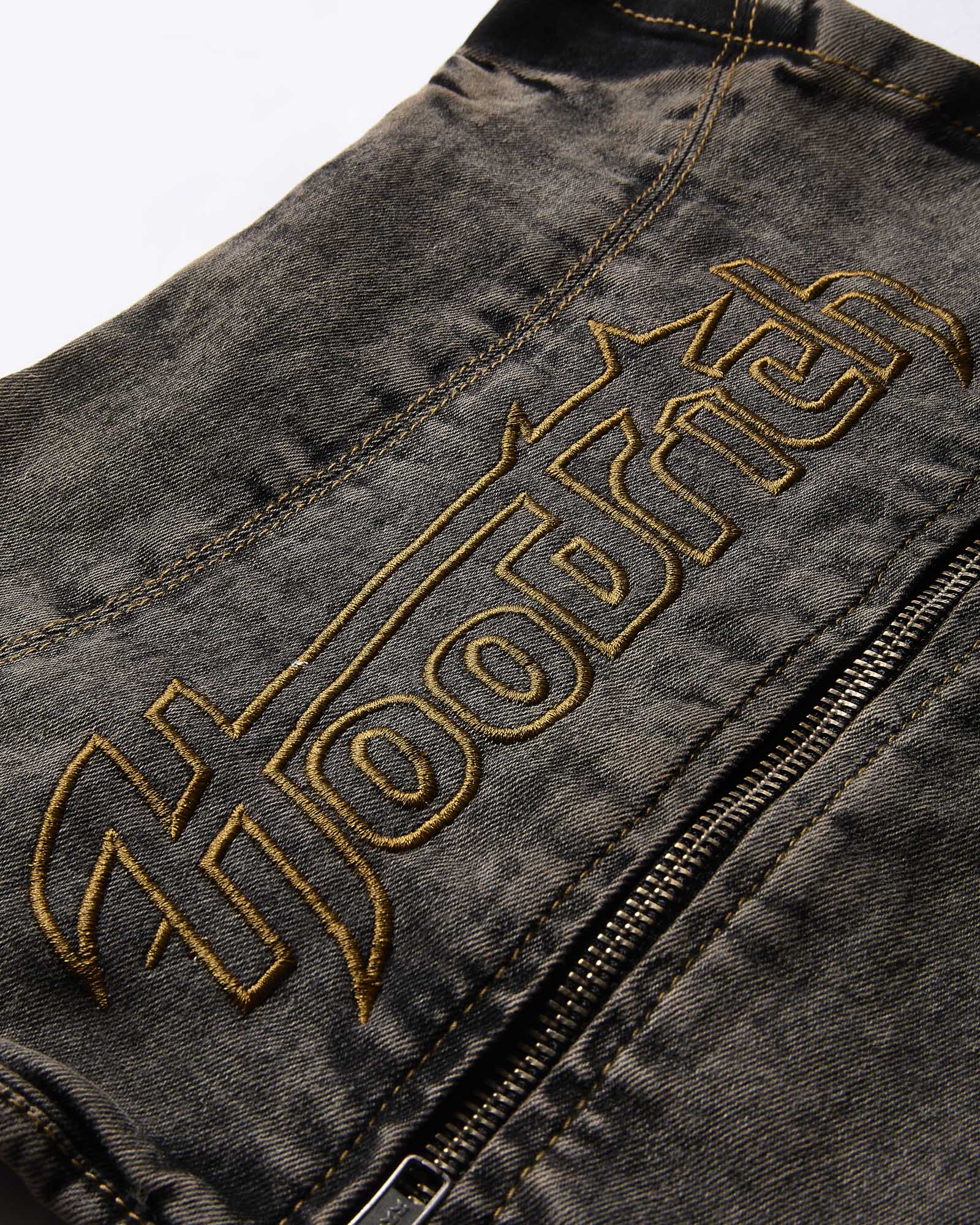 Close-up of the yellow Hoodrich logo embroidery on the black denim fabric of the corset top.