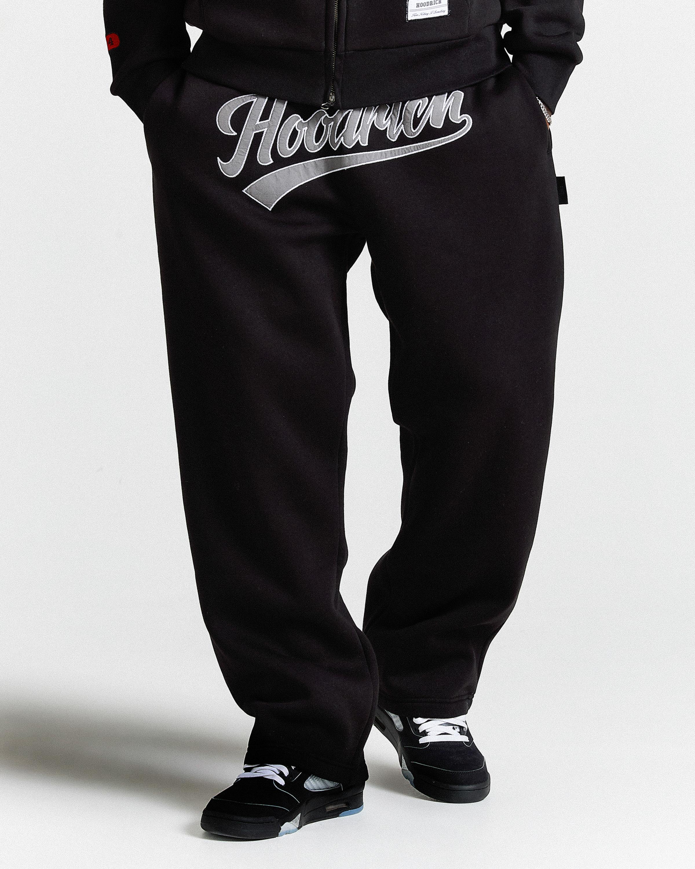 Black pants with 'Hoodman' logo worn by a person on a white background