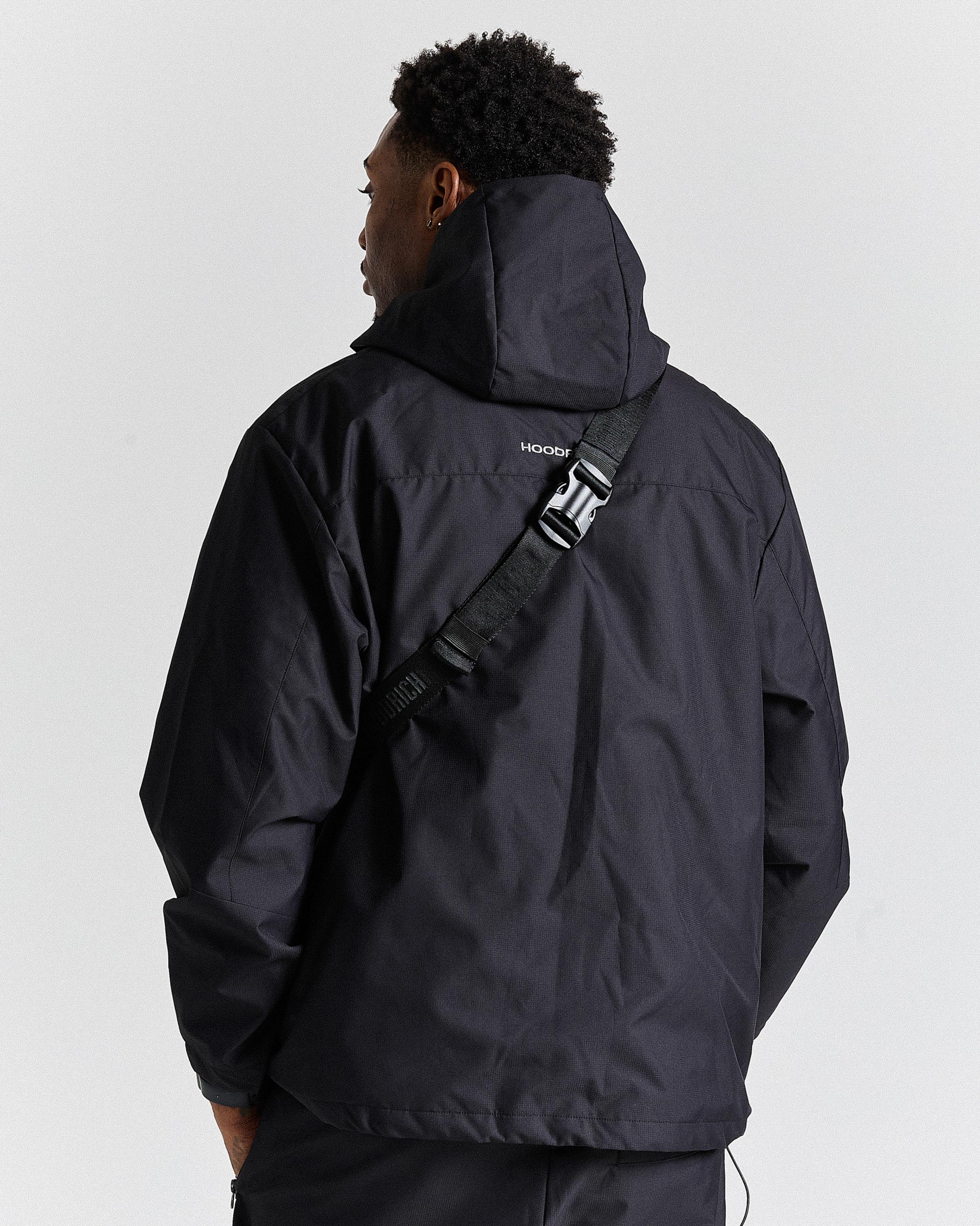 Person wearing a black jacket with a visible brand logo on a light gray background