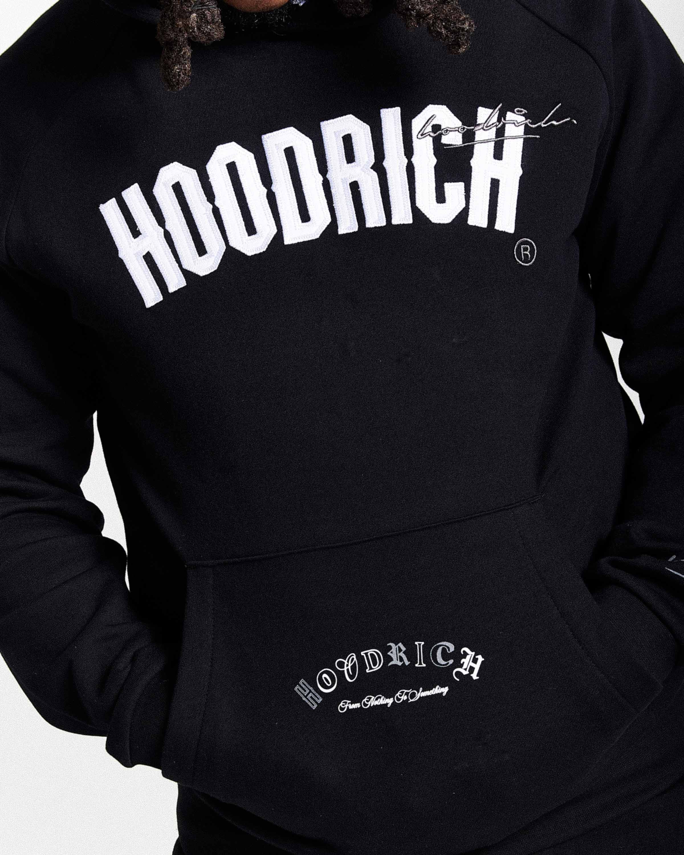 Displays a model wearing the Black 'Hoodrich' branded men's Stature Full Tracksuit