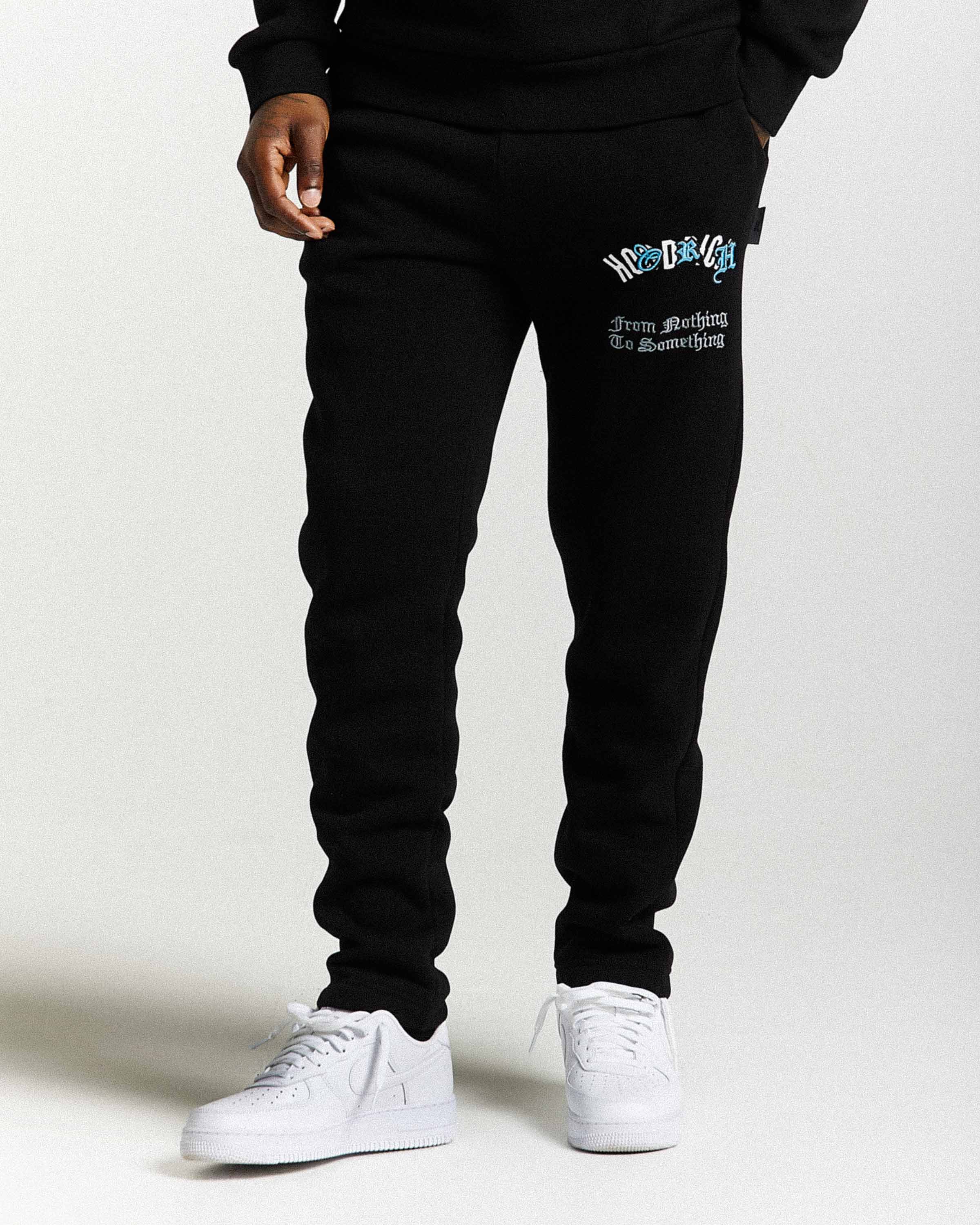 Displays a model wearing the Black 'Hoodrich' branded men's Shadow Full Tracksuit