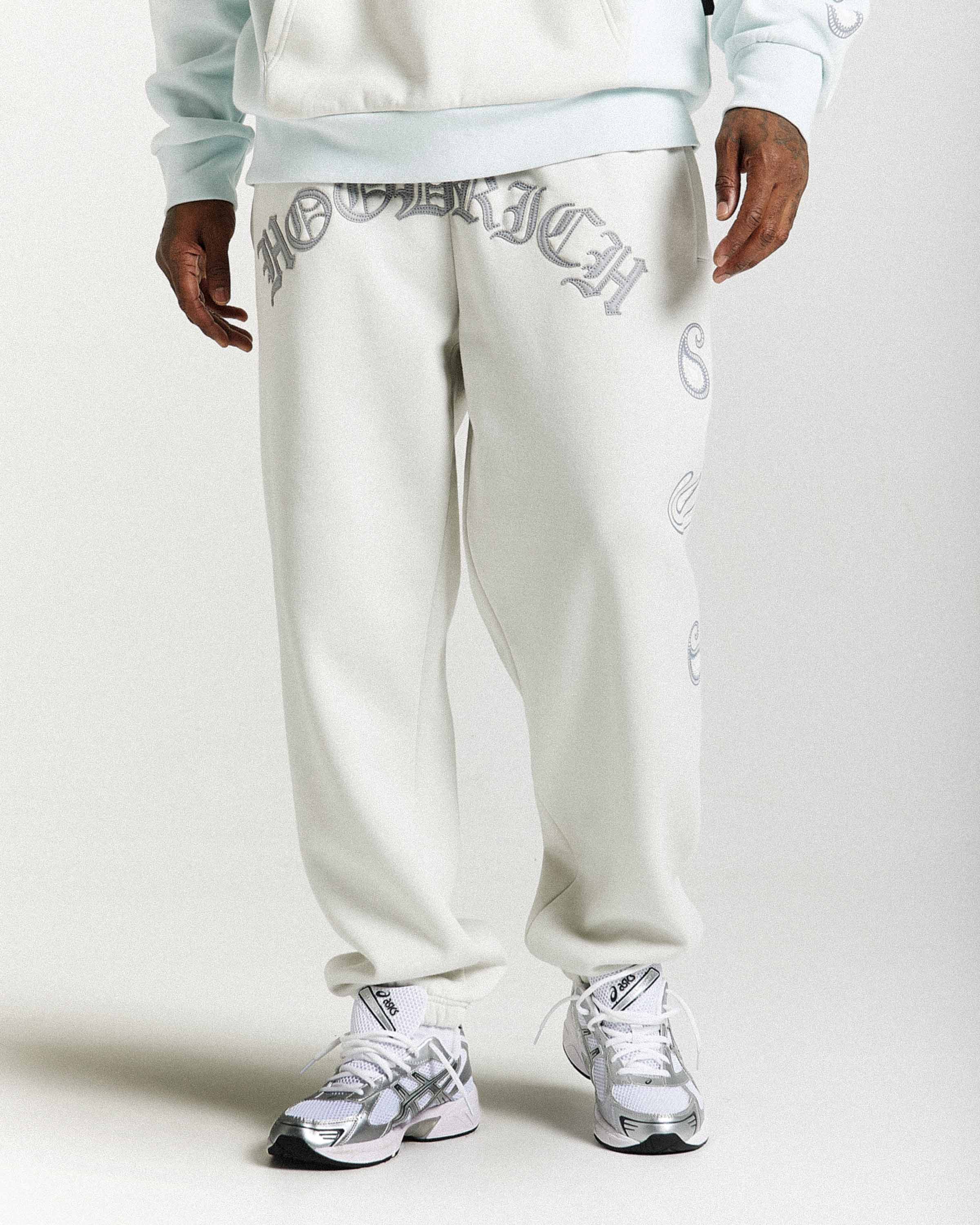 Person wearing light gray sweatpants with branding on a white background