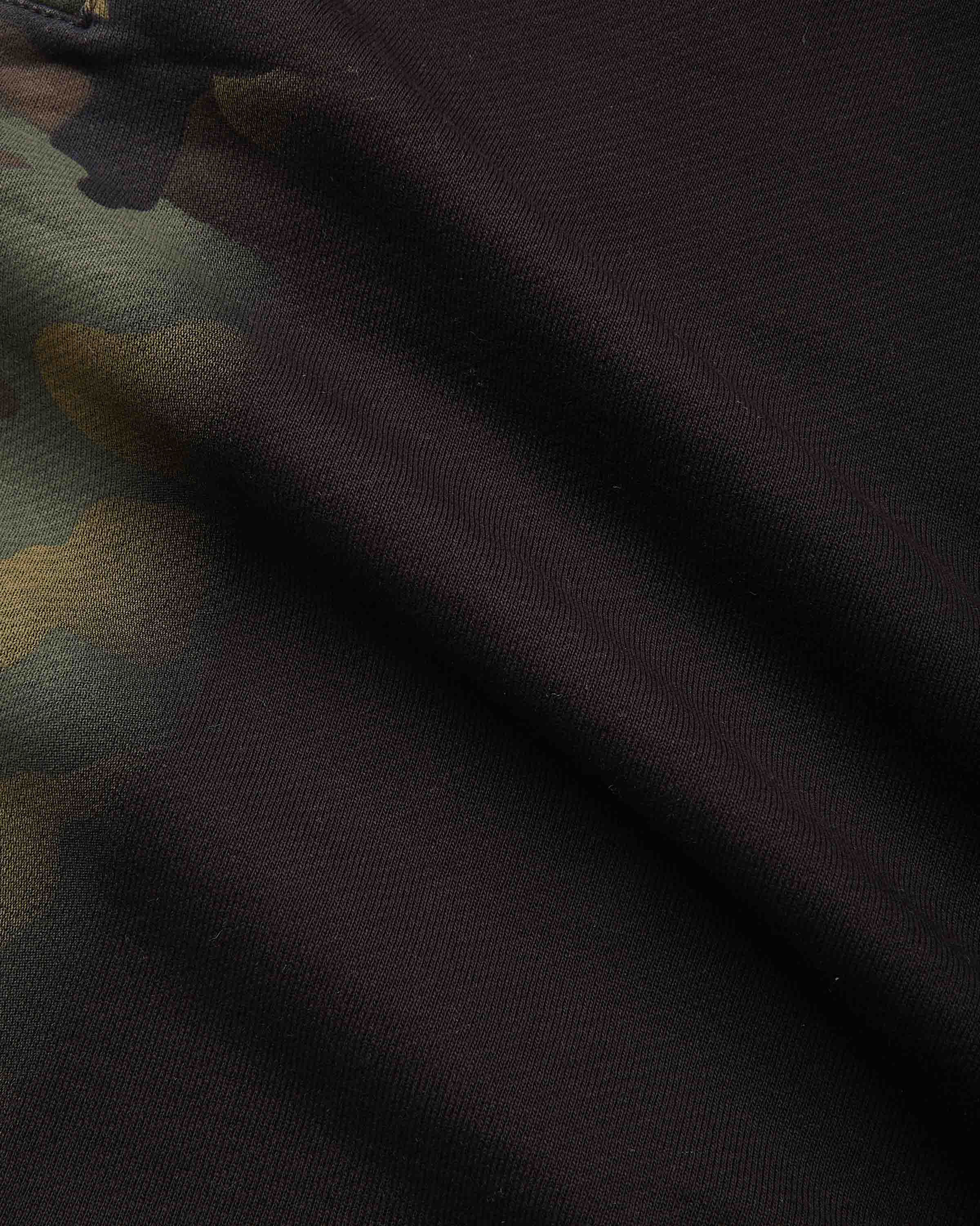 Close-up of dark camouflage fabric with a solid black or very deep charcoal section and partial olive green and tan camo areas visible on the left.