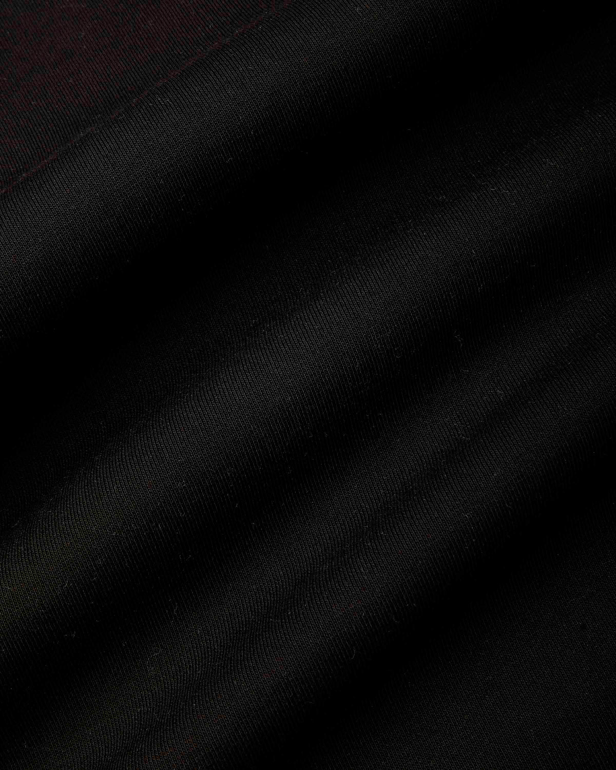 A close-up of a black fabric texture with soft diagonal folds and a subtle sheen.
