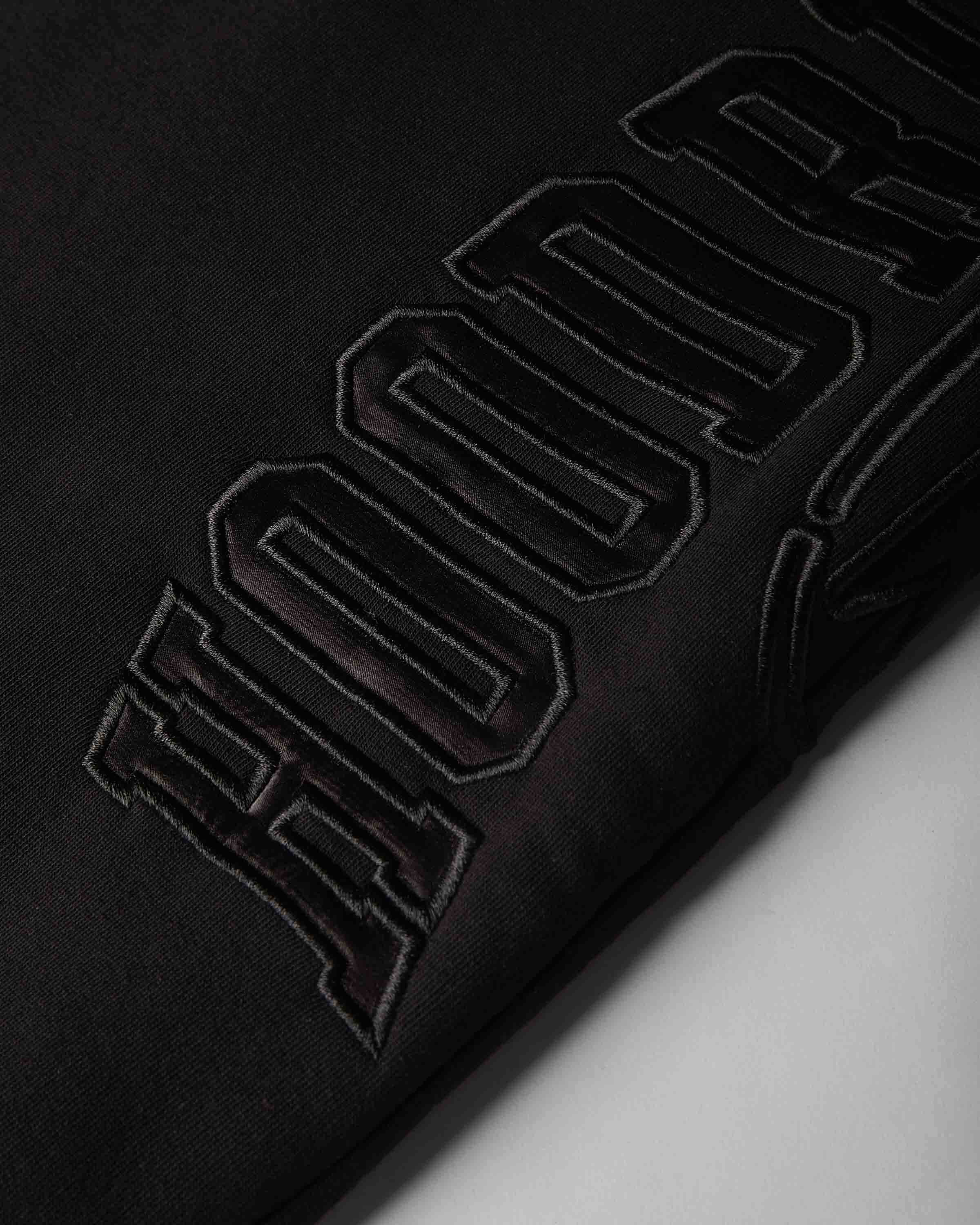 Close-up of a black fabric surface with large tonal embroidered lettering running diagonally across the frame.