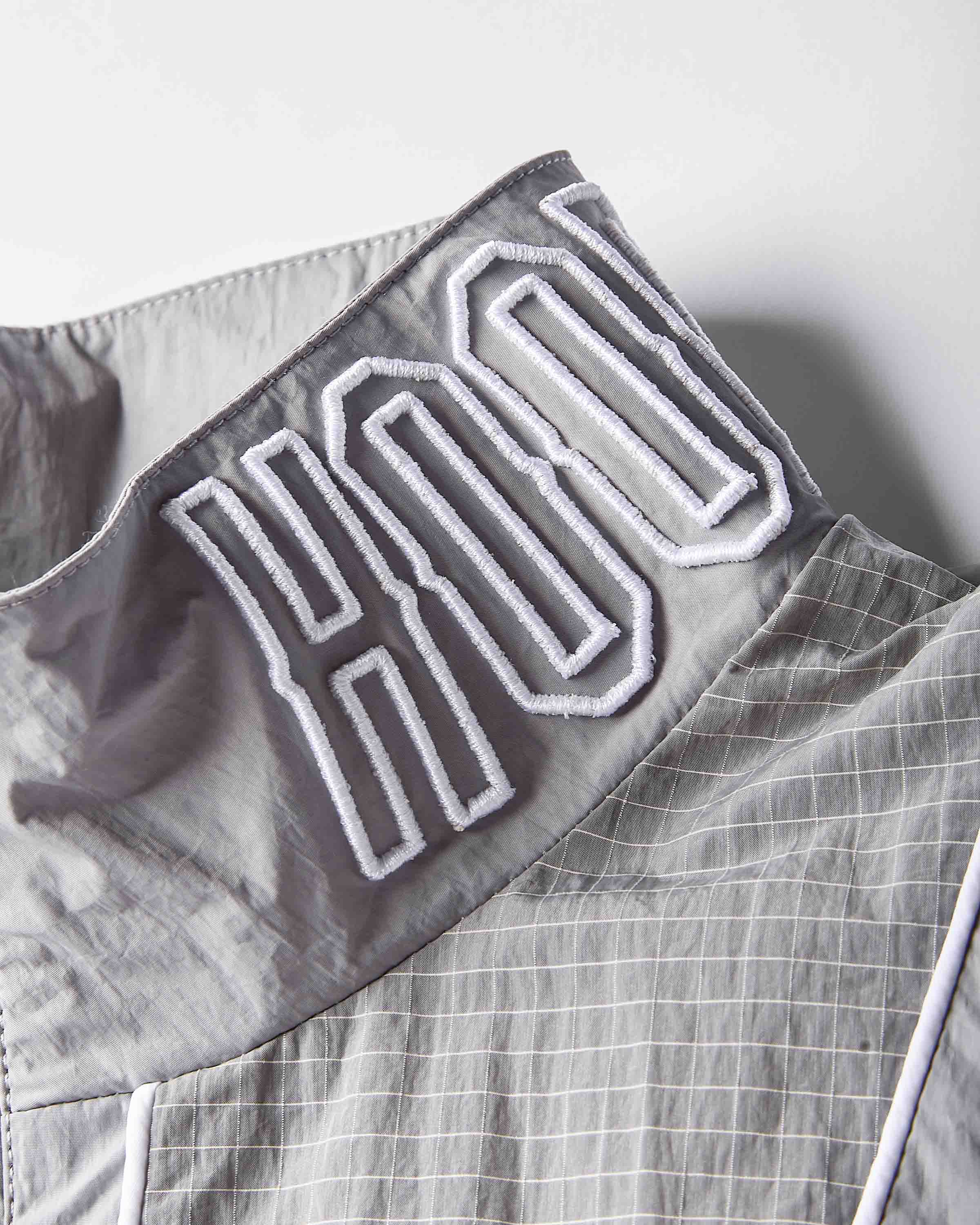 Close-up of a gray lightweight fabric garment with a high collar featuring large white embroidered lettering outlined in black.