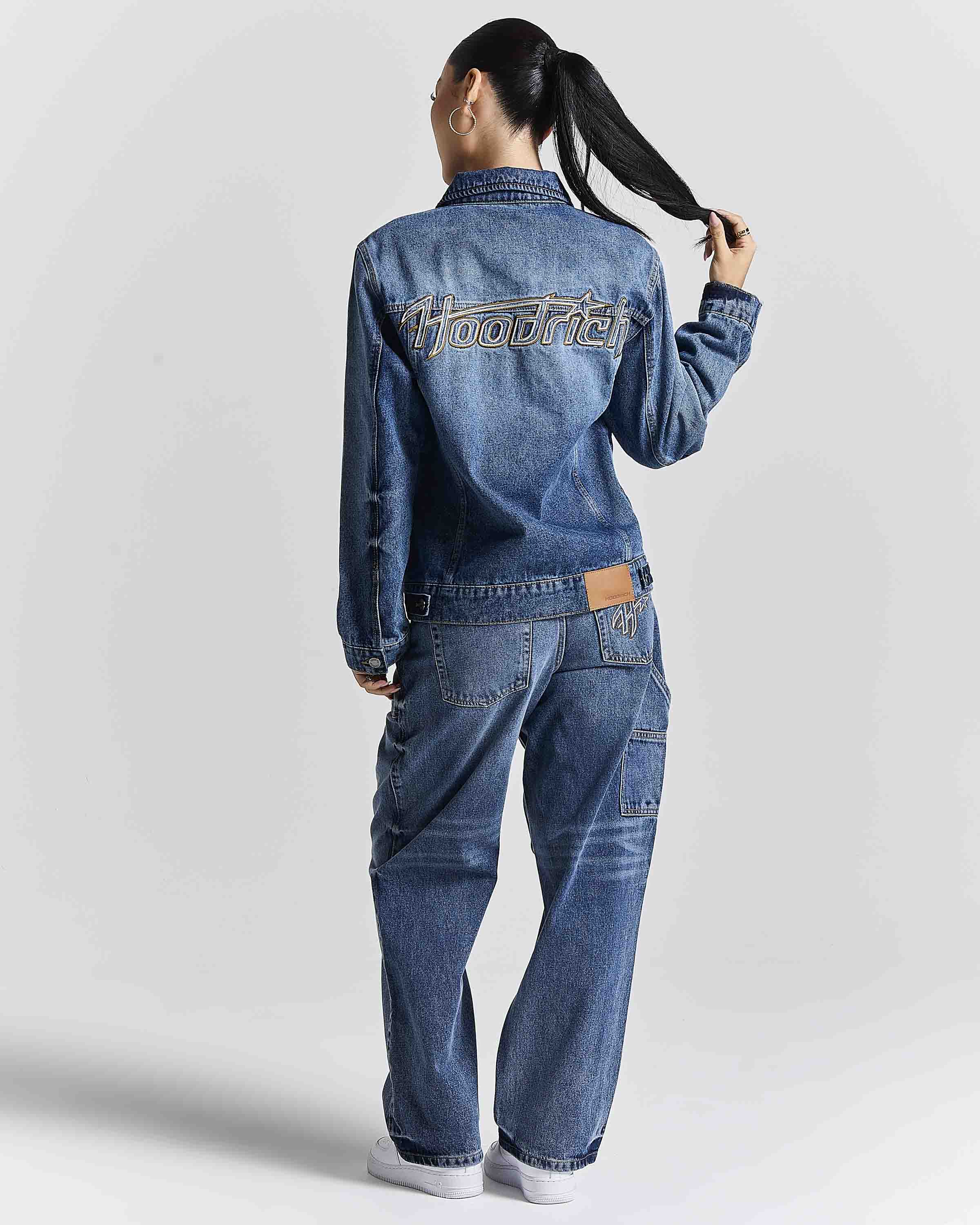 A model shown from the back wearing a blue denim jacket and matching wide-leg denim jeans. The jacket features 'hoodster' embroidered in white across the upper back, and a brown leather brand patch is visible on the back waistband.