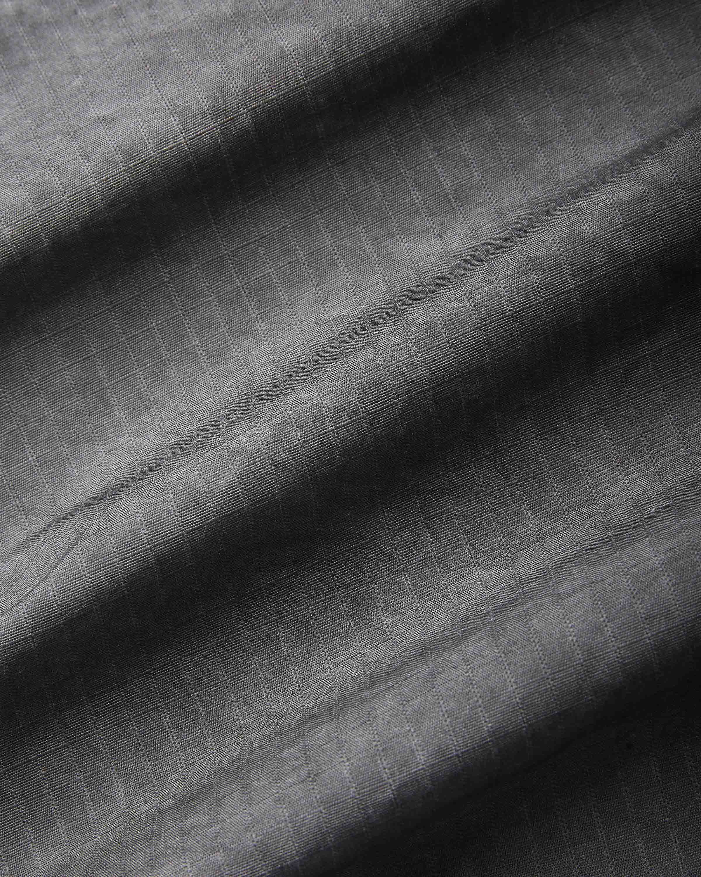 A close-up of dark gray textured fabric with a subtle woven grid pattern and soft diagonal folds.