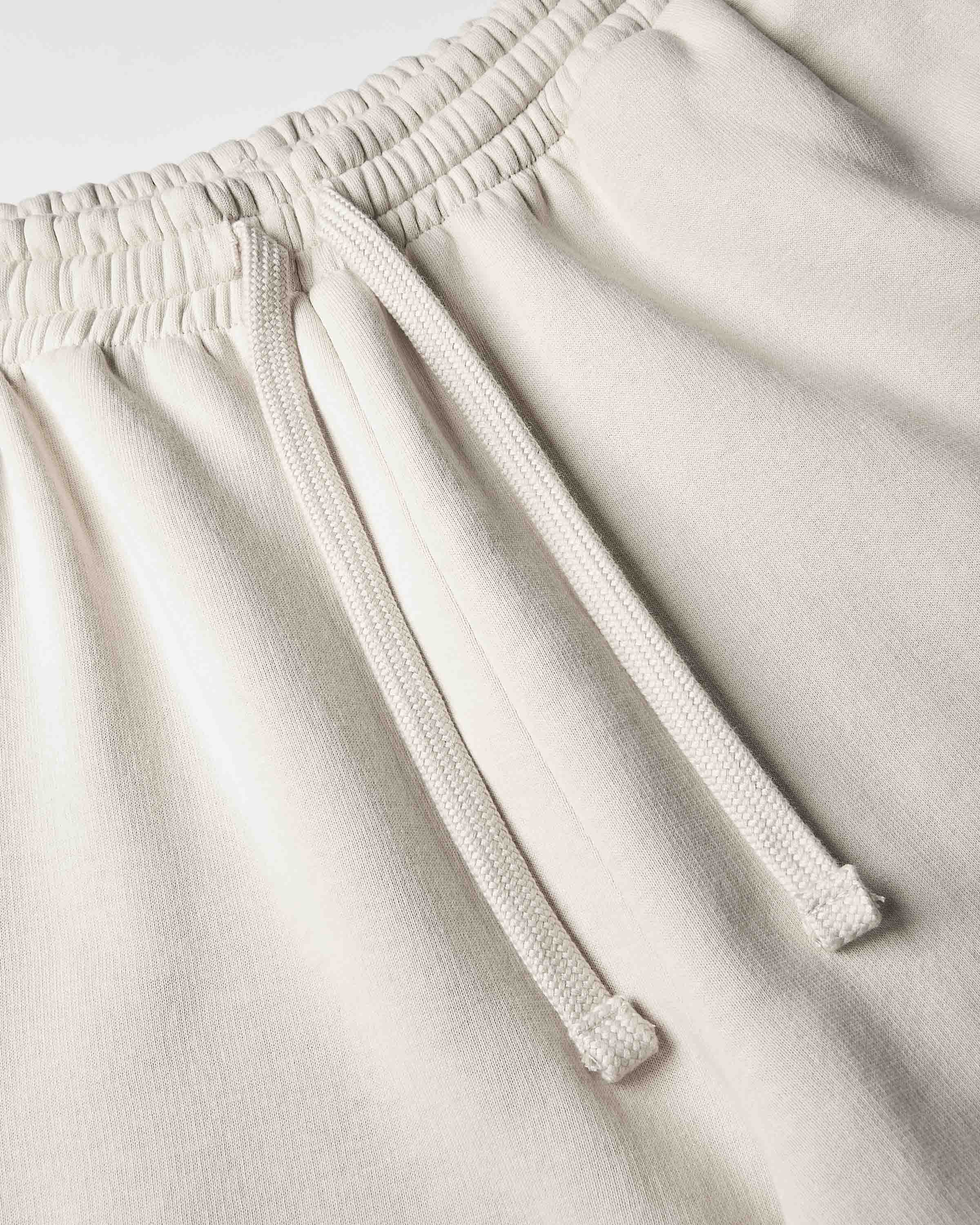 Close-up of a pair of light beige or cream-colored sweatpants, showing the elastic waistband and matching drawstring.