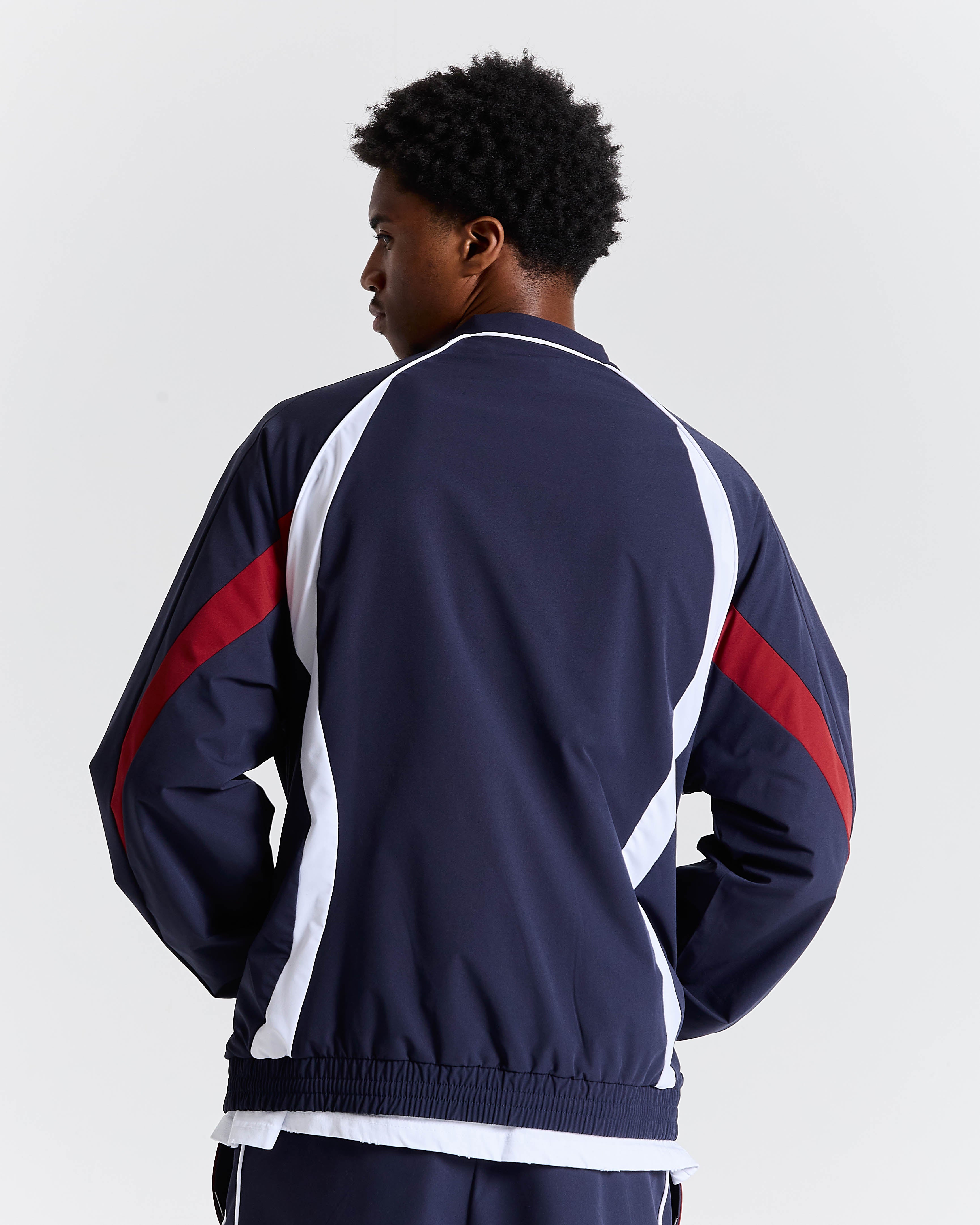 Person wearing a navy tracksuit with red and white accents on a light gray background