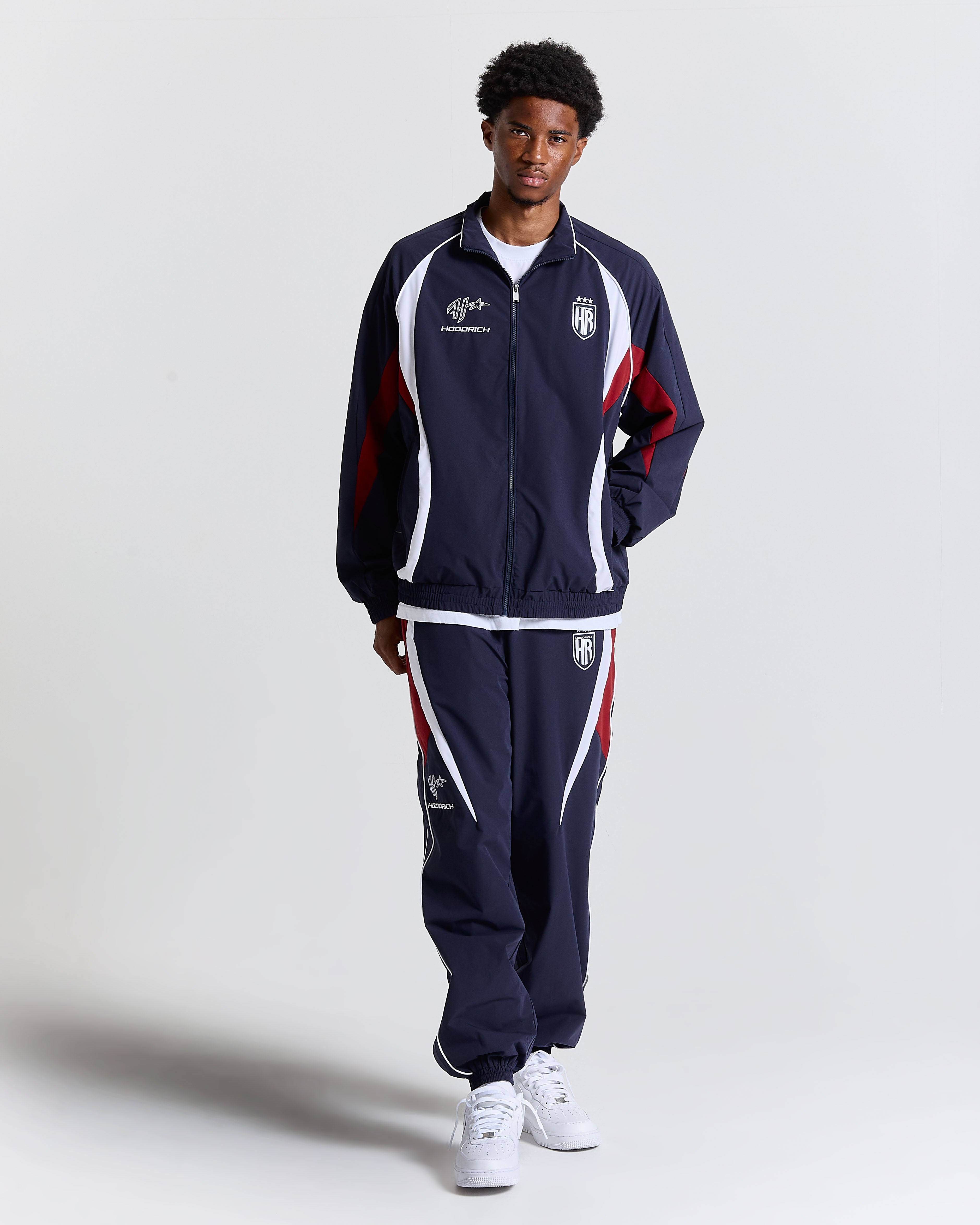 Person wearing a navy tracksuit with red and white accents on a light gray background