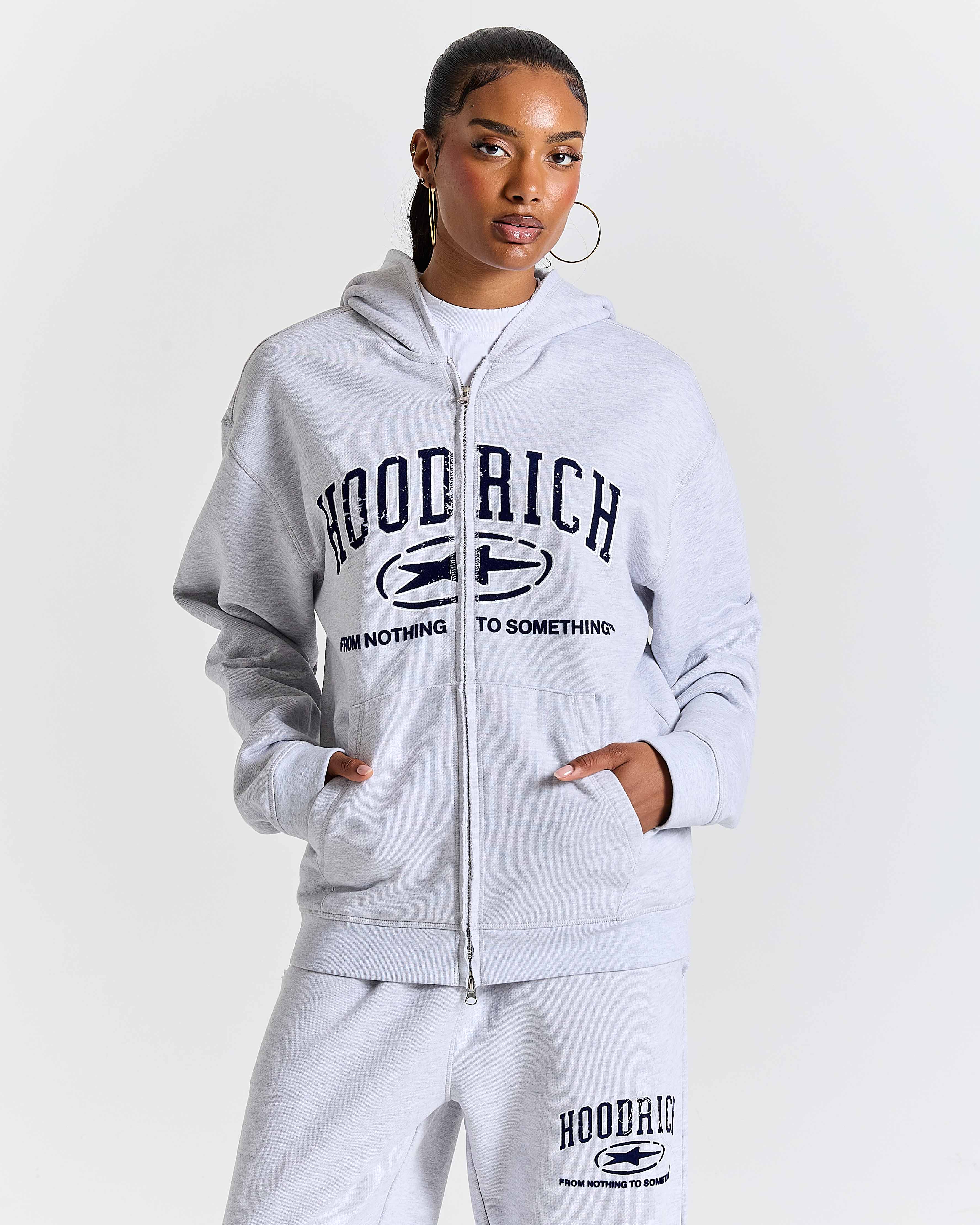 Person wearing a gray 'Hoodrich' tracksuit on a white background