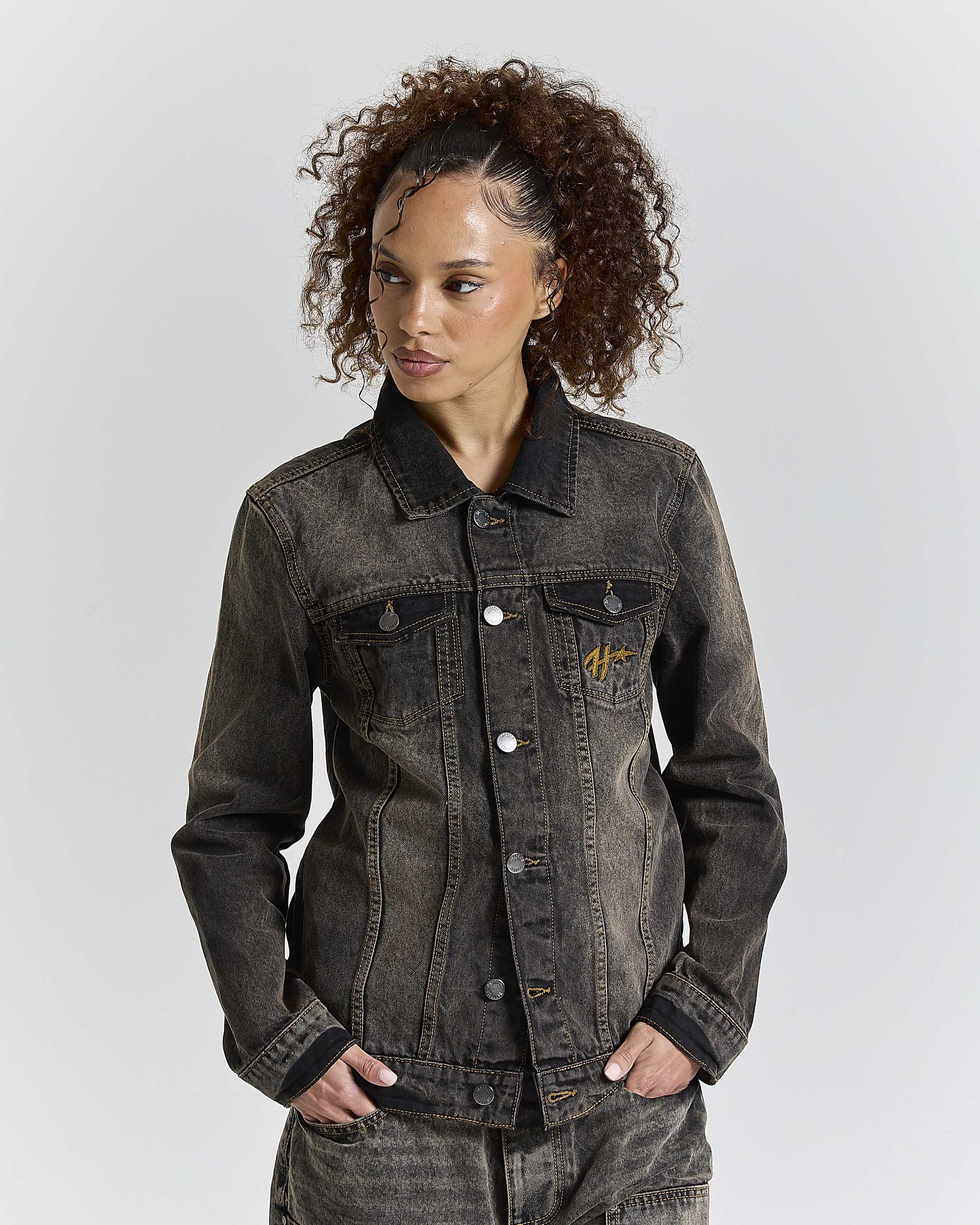 Woman wearing a dark denim jacket with a brand logo on a light gray background