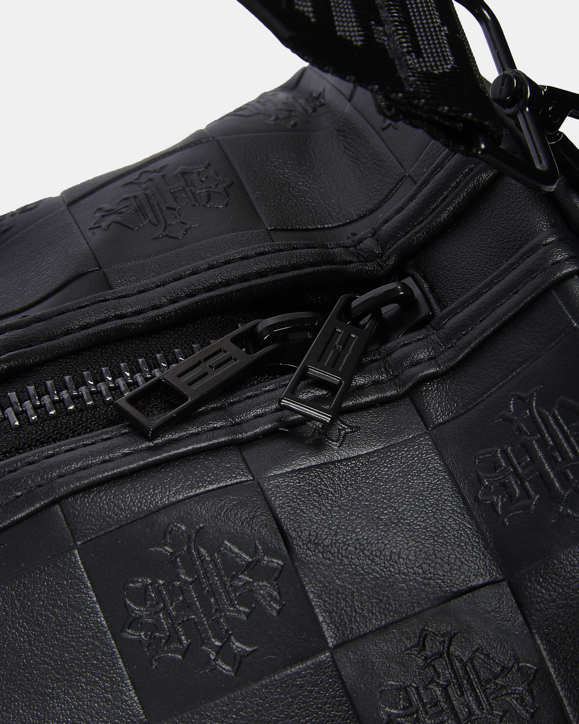 Close-up of a black leather bag with embossed patterns and zippers.