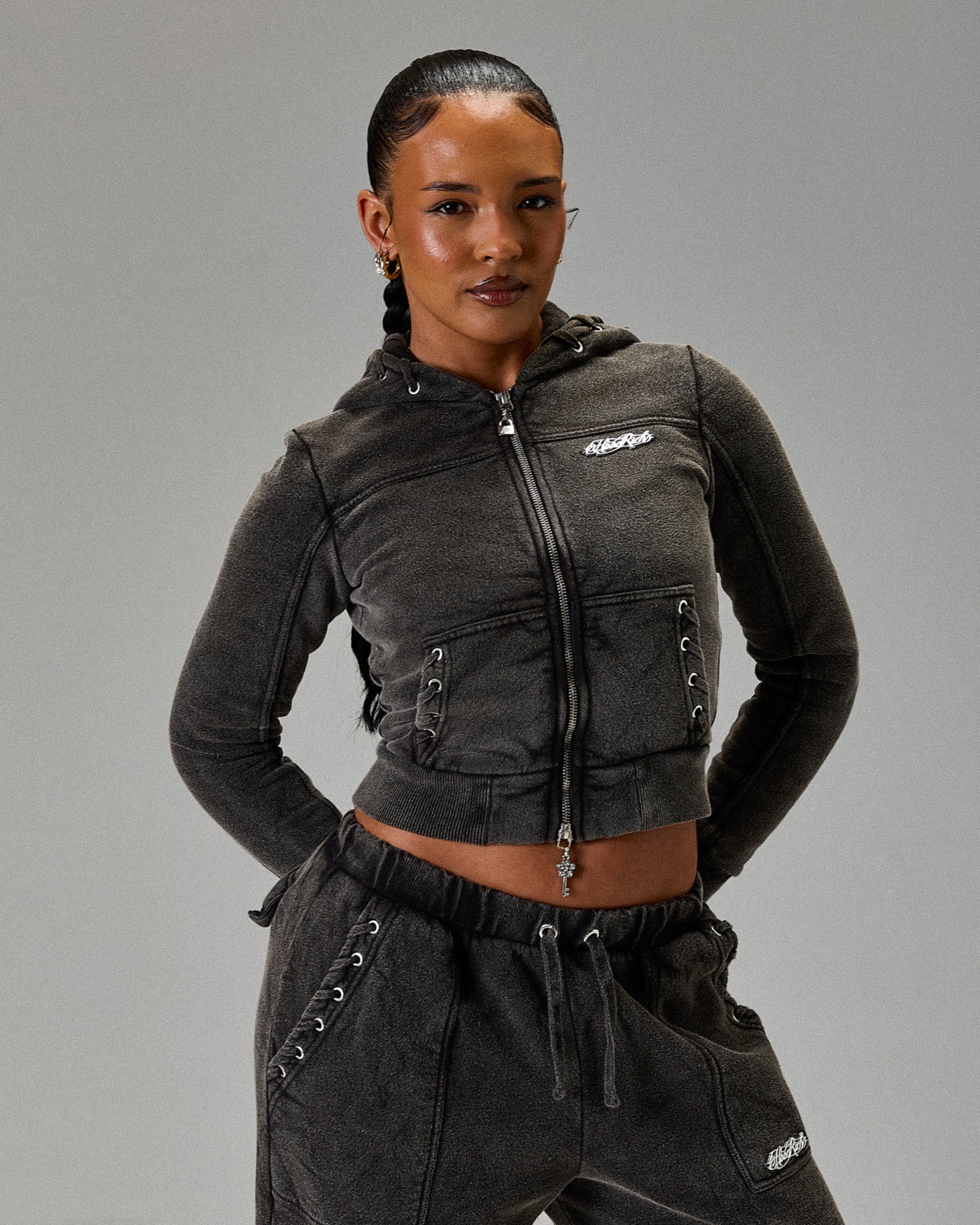 Person wearing a dark gray hoodie and pants with a logo on a gray background