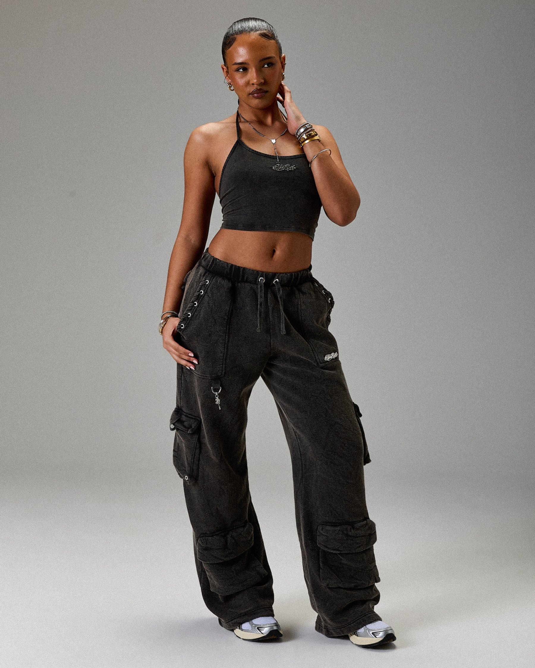 Woman wearing black athletic outfit with cargo pants on a gray background