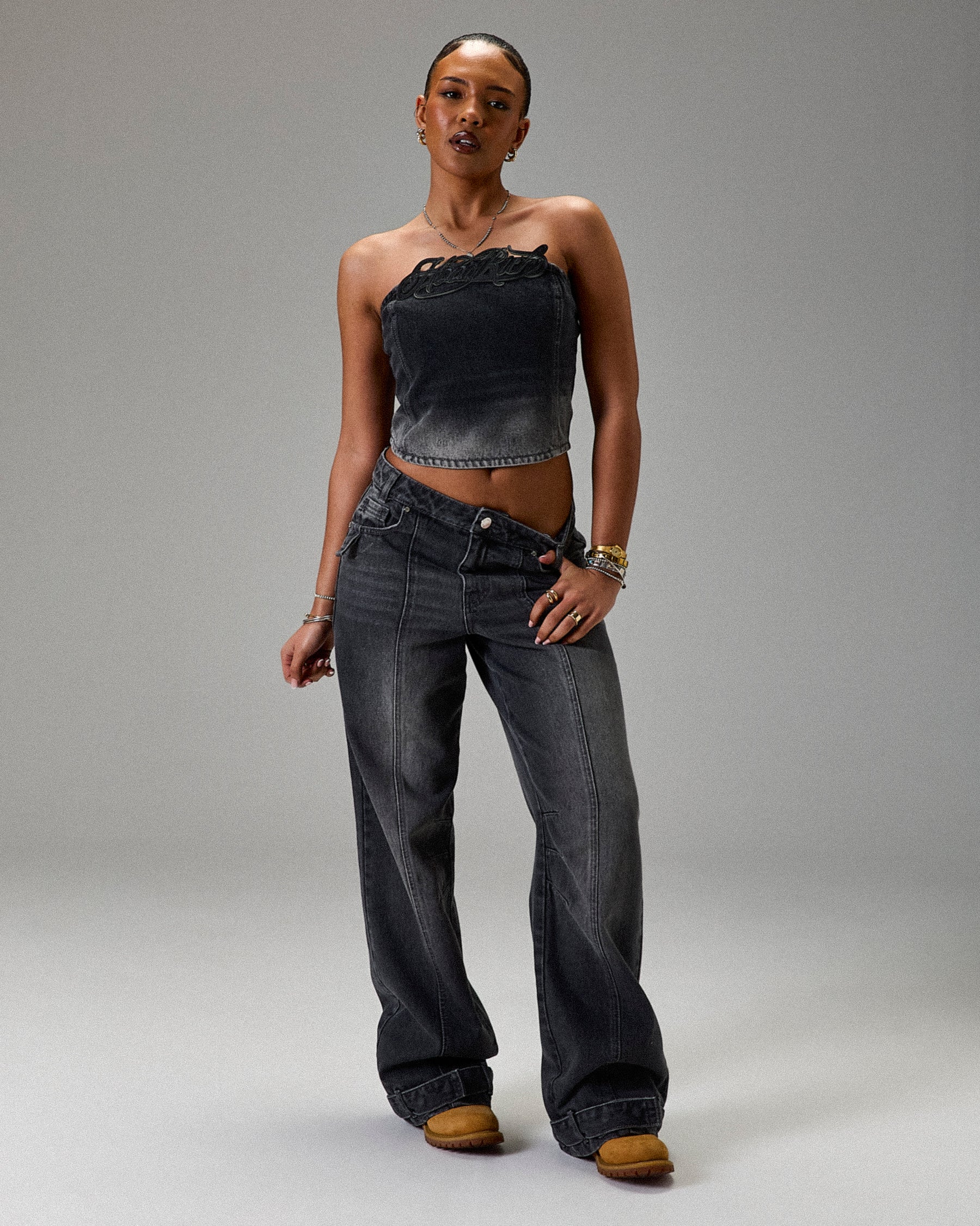 Woman wearing a strapless top and jeans on a gray background