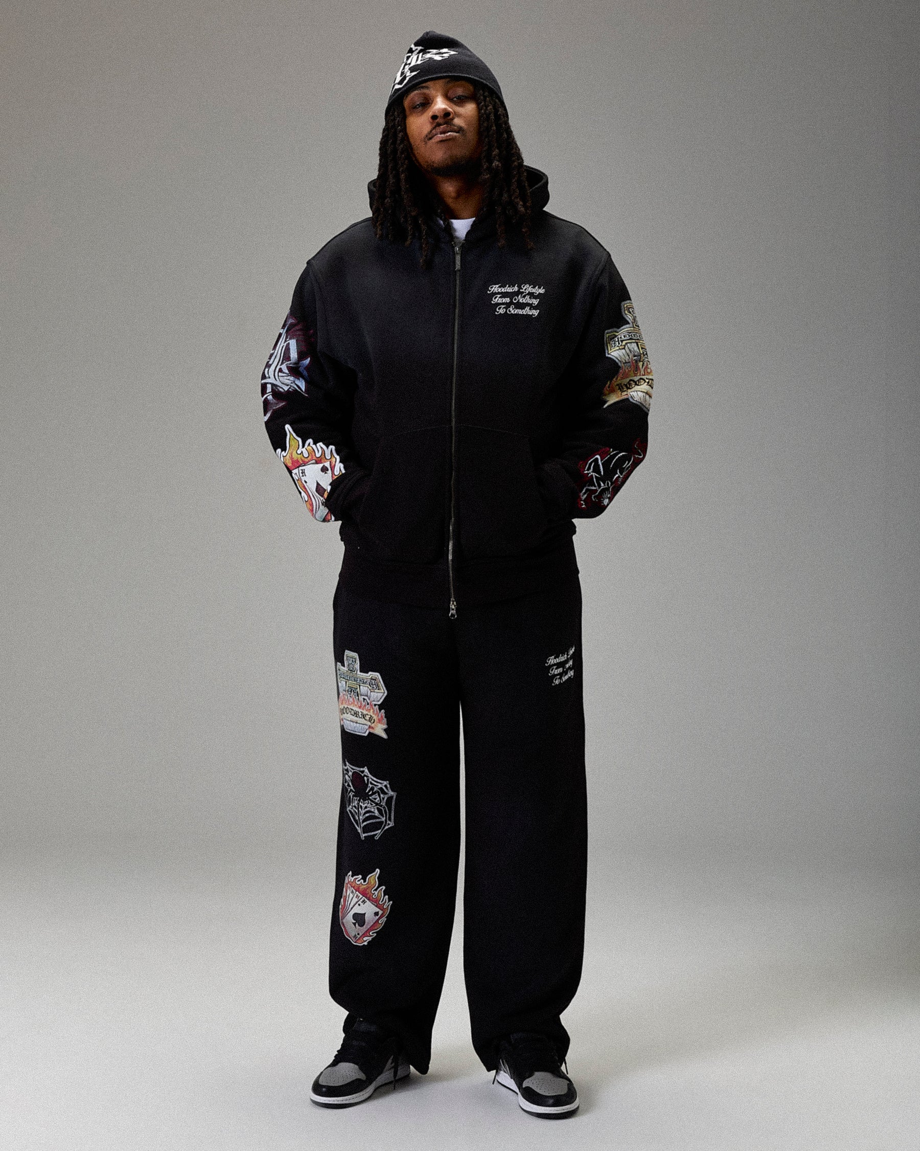 Person wearing a black tracksuit with colorful designs on a gray background