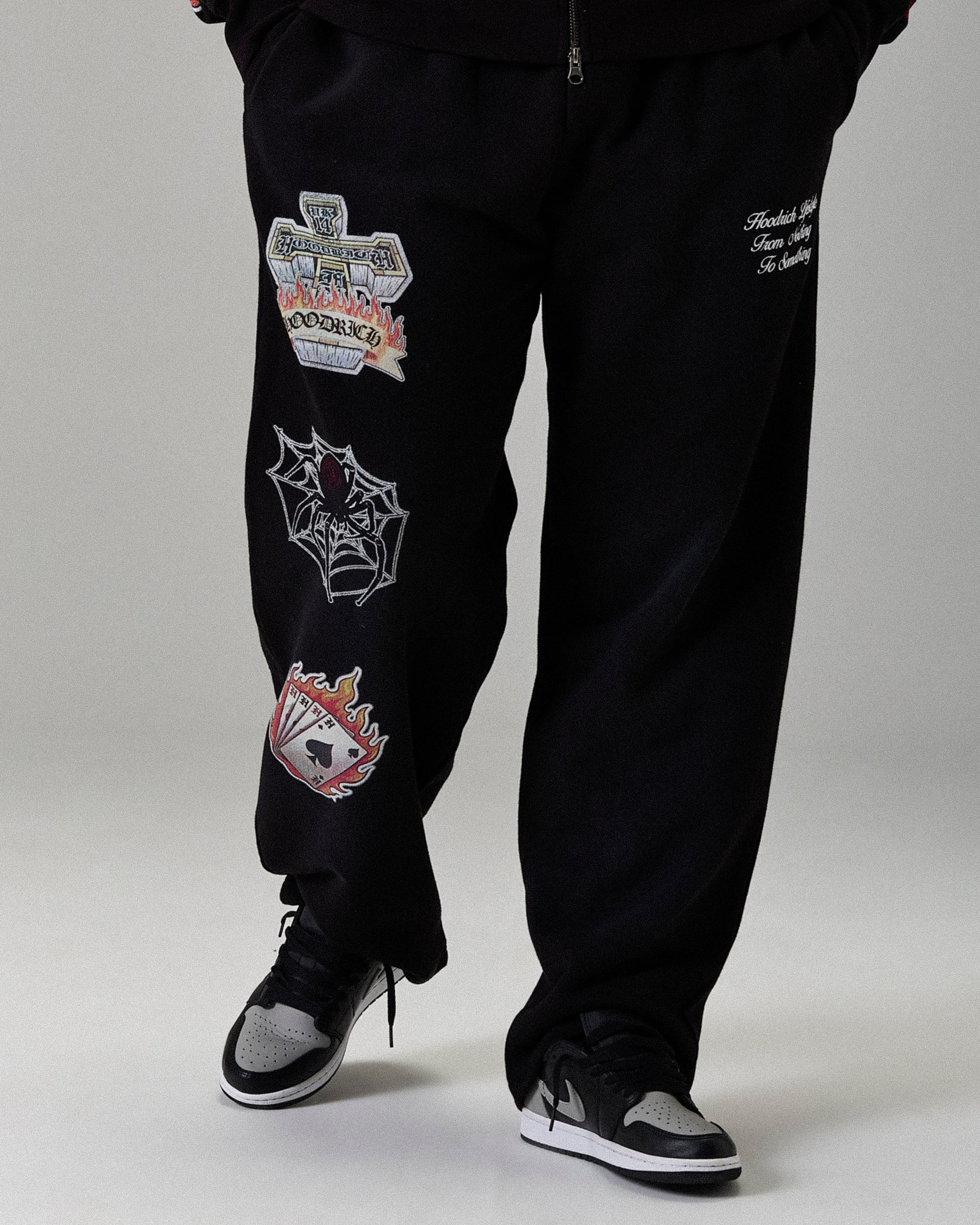 Black sweatpants with patches worn by a person on a plain background