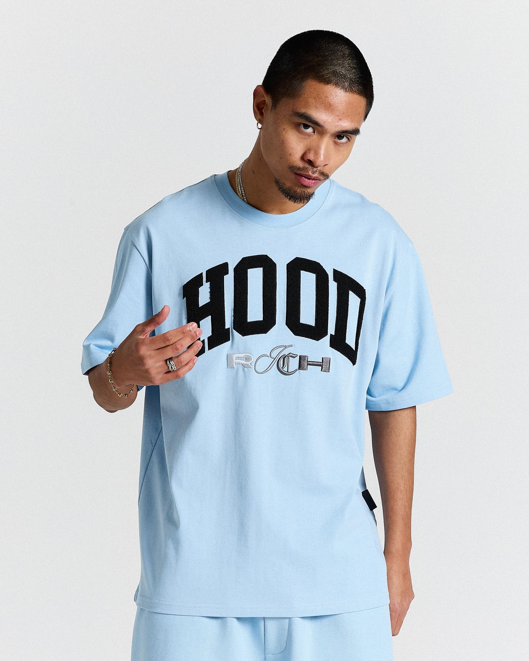 Person wearing a light blue t-shirt with 'HOODRICH' text on a plain background