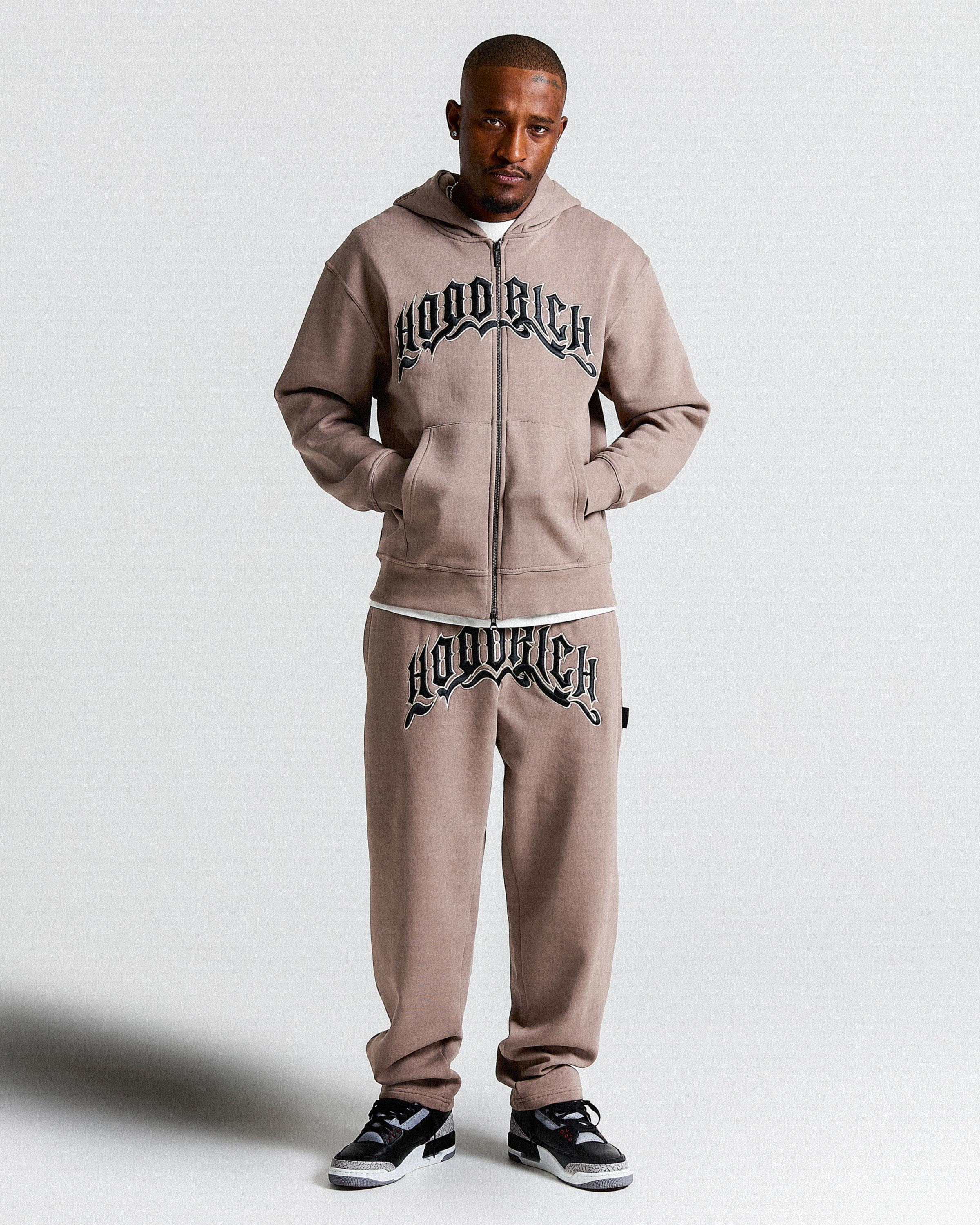 Man wearing a beige tracksuit with 'Hoodrich' branding on a white background