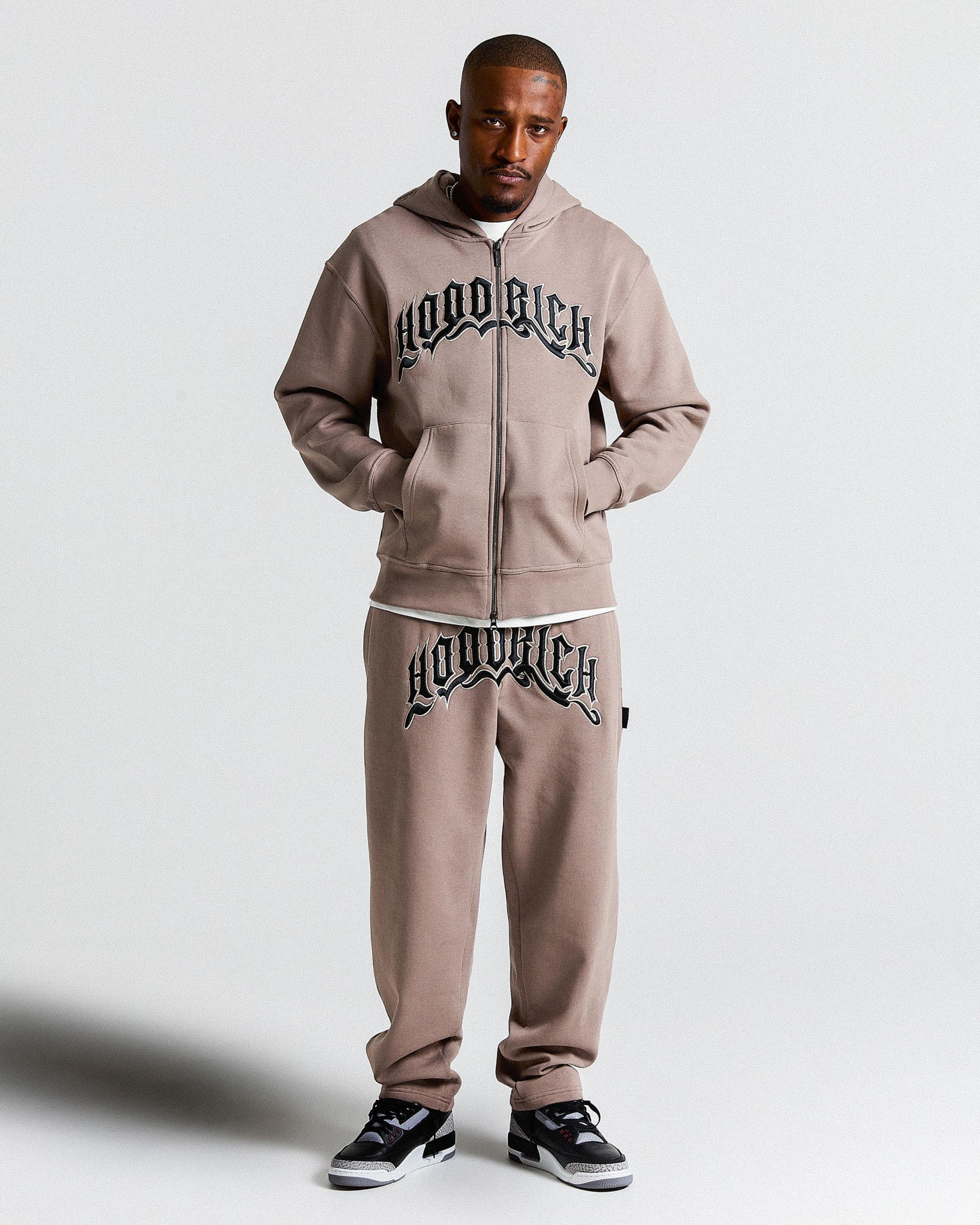 Man wearing a brown tracksuit with 'Hoodrich' branding on a white background
