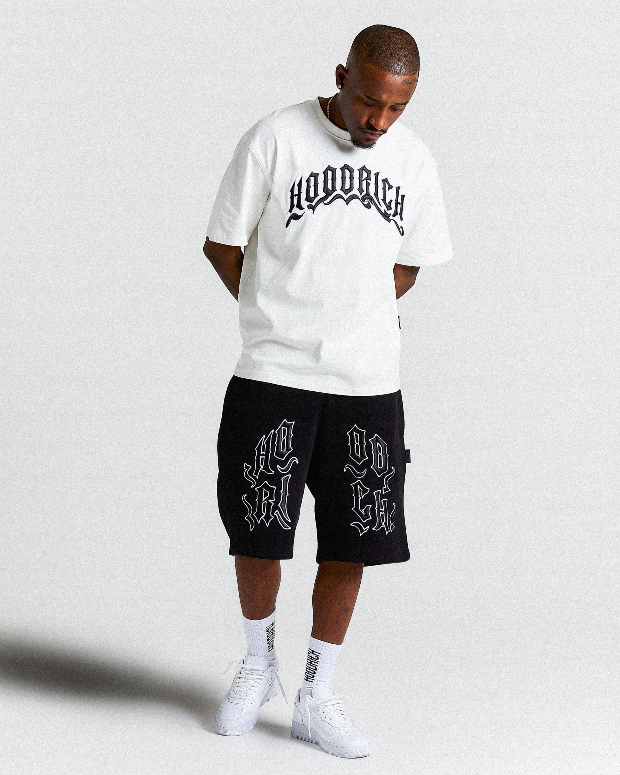 Man wearing a white t-shirt and black shorts with 'Hoodrich' branding on a light gray background