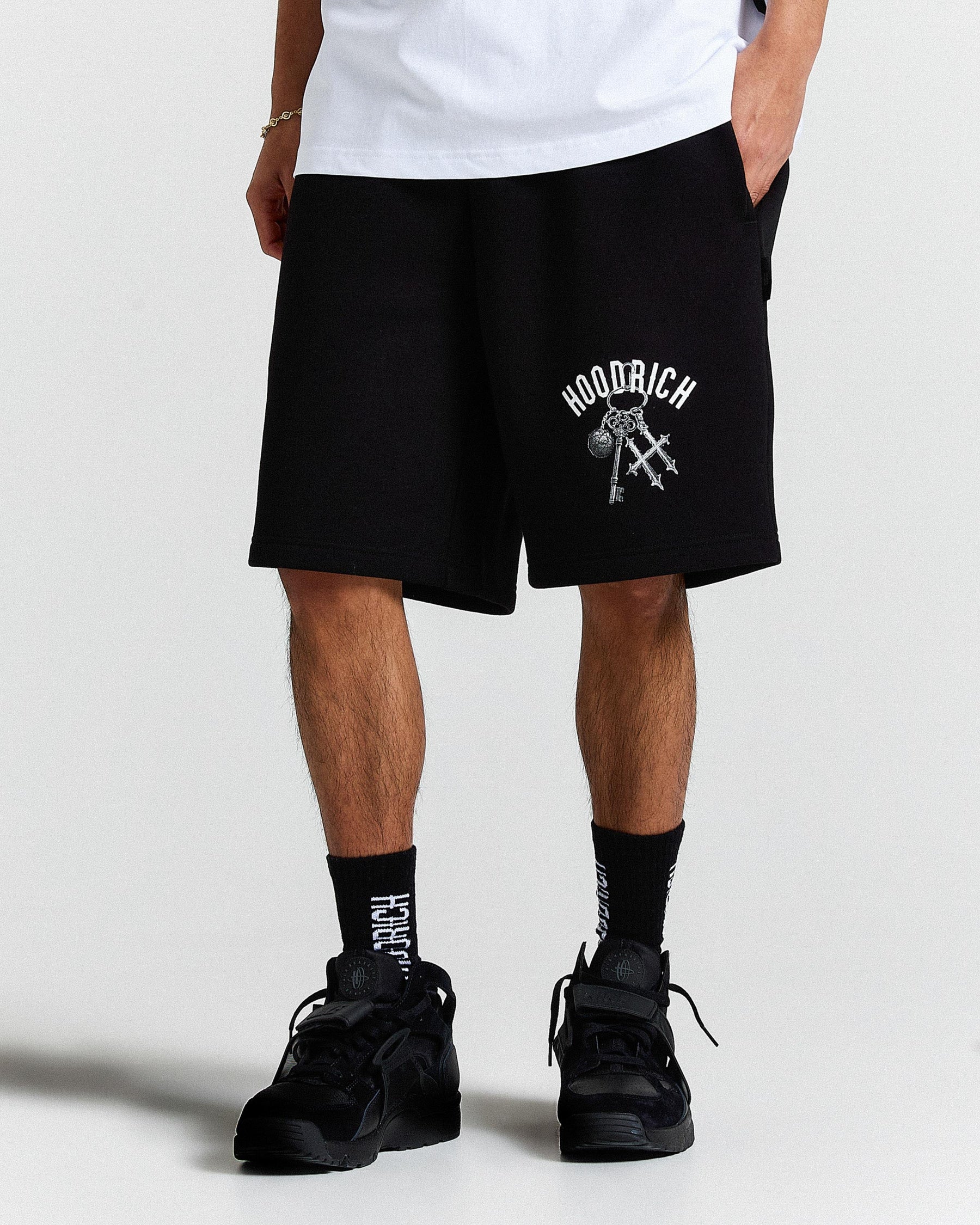 Person wearing black shorts with a logo and text, standing against a white background