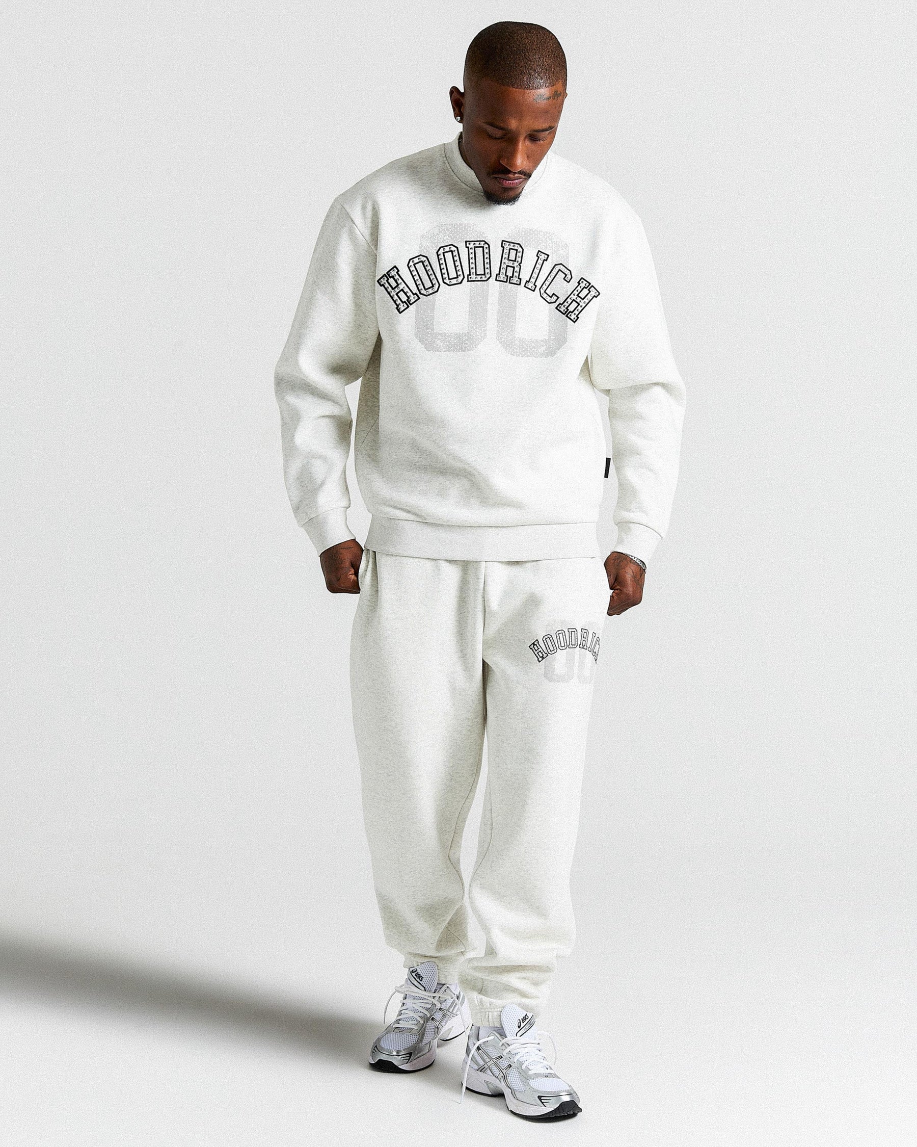Man wearing a white 'HOODRICH' tracksuit on a light gray background