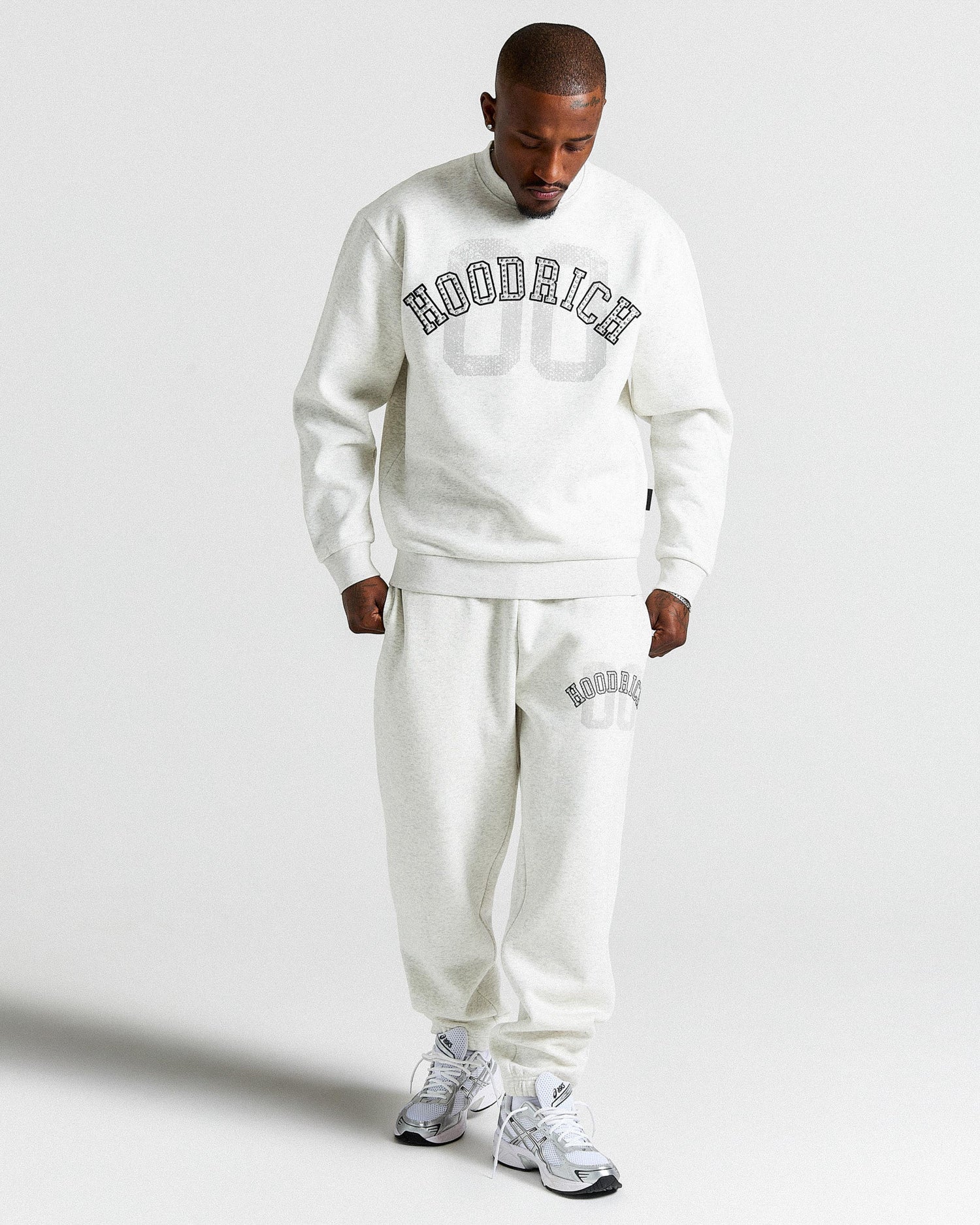 Man wearing a light grey 'HOODRICH' tracksuit on a plain background