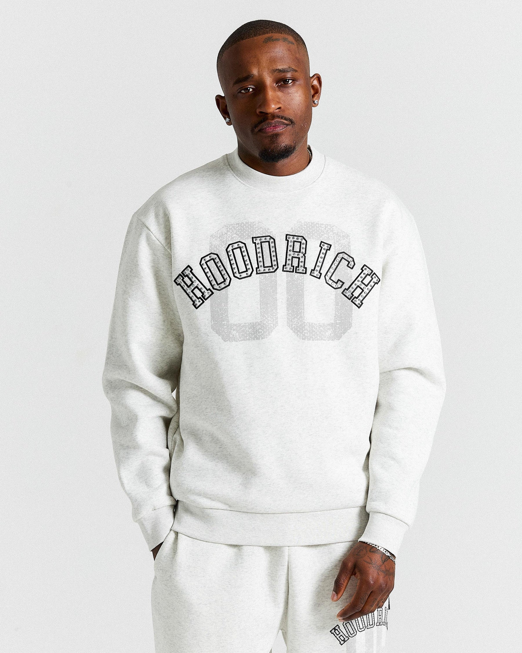 Man wearing a light grey 'Hood Rich' sweatshirt on a plain background
