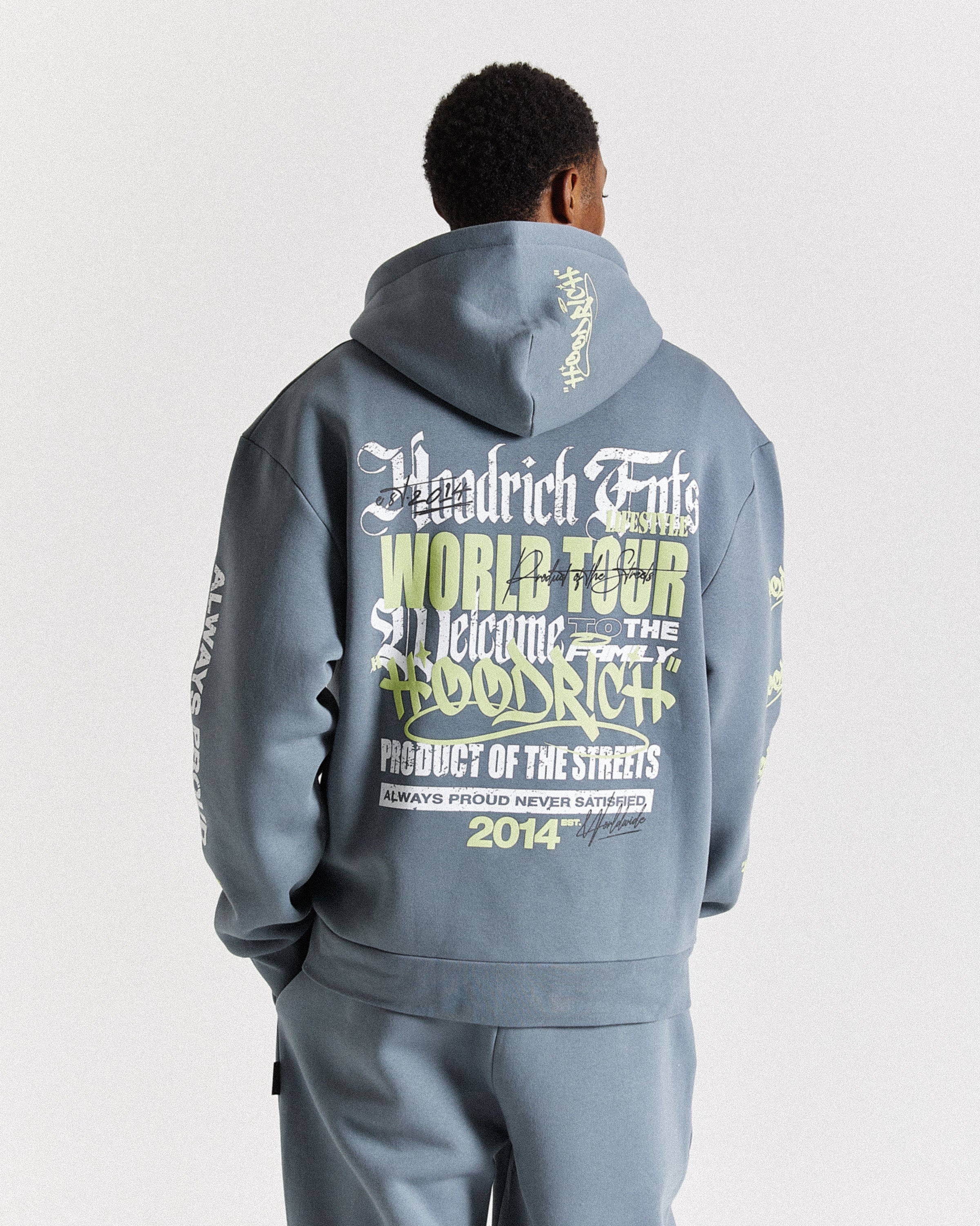 A man viewed from behind wearing a slate blue-gray Woodrich Endz World Tour hoodie with large graphic text on the back, paired with matching pants, against a light gray studio background.