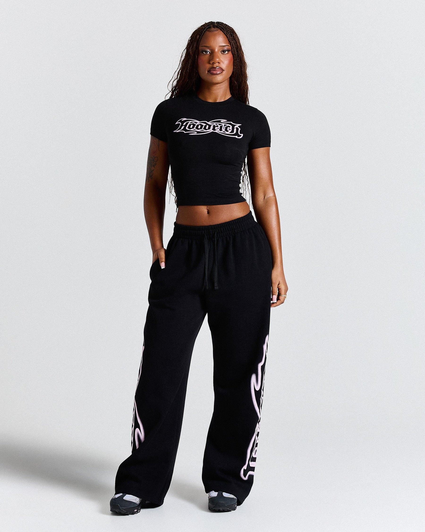 Woman wearing a black crop top and black pants with white designs on a light gray background