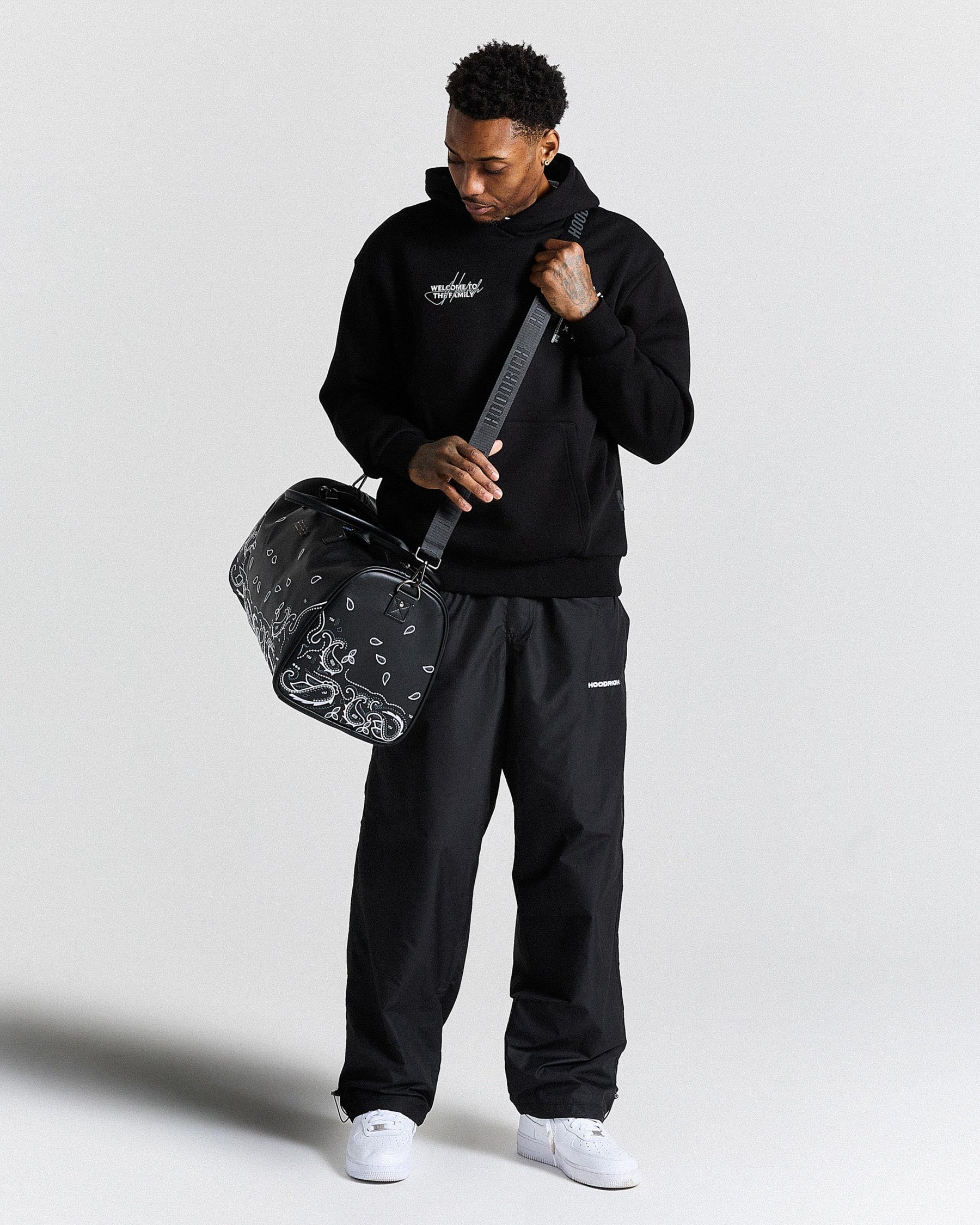 Man holding a black duffel bag with a bandana design against a light gray background