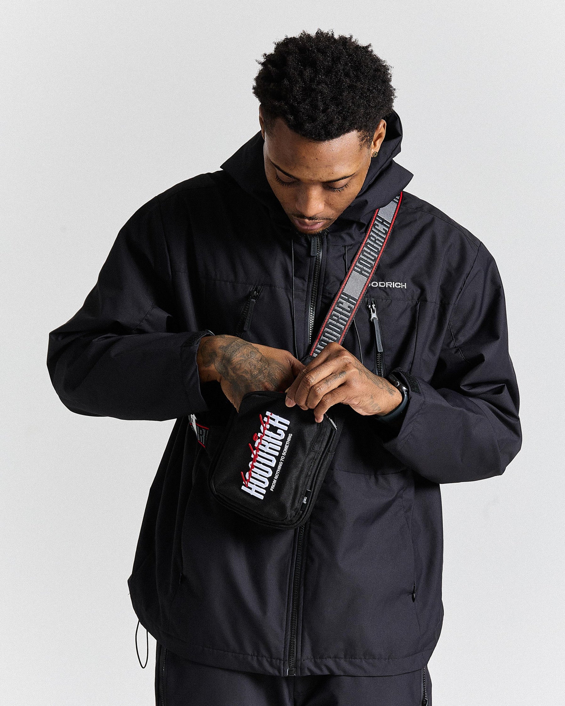 Person wearing a black jacket with a visible brand logo, holding a black bag with a strap.