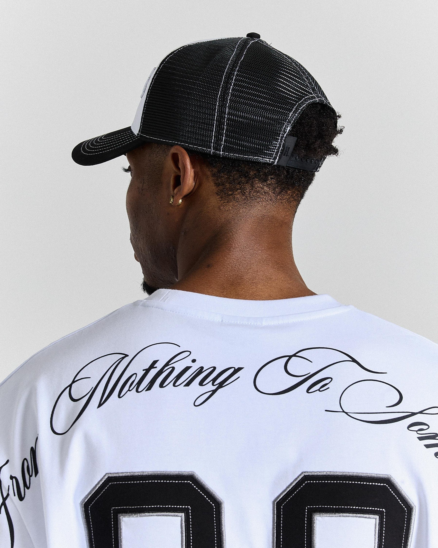 Person wearing a white t-shirt with black text and a black cap on a plain background