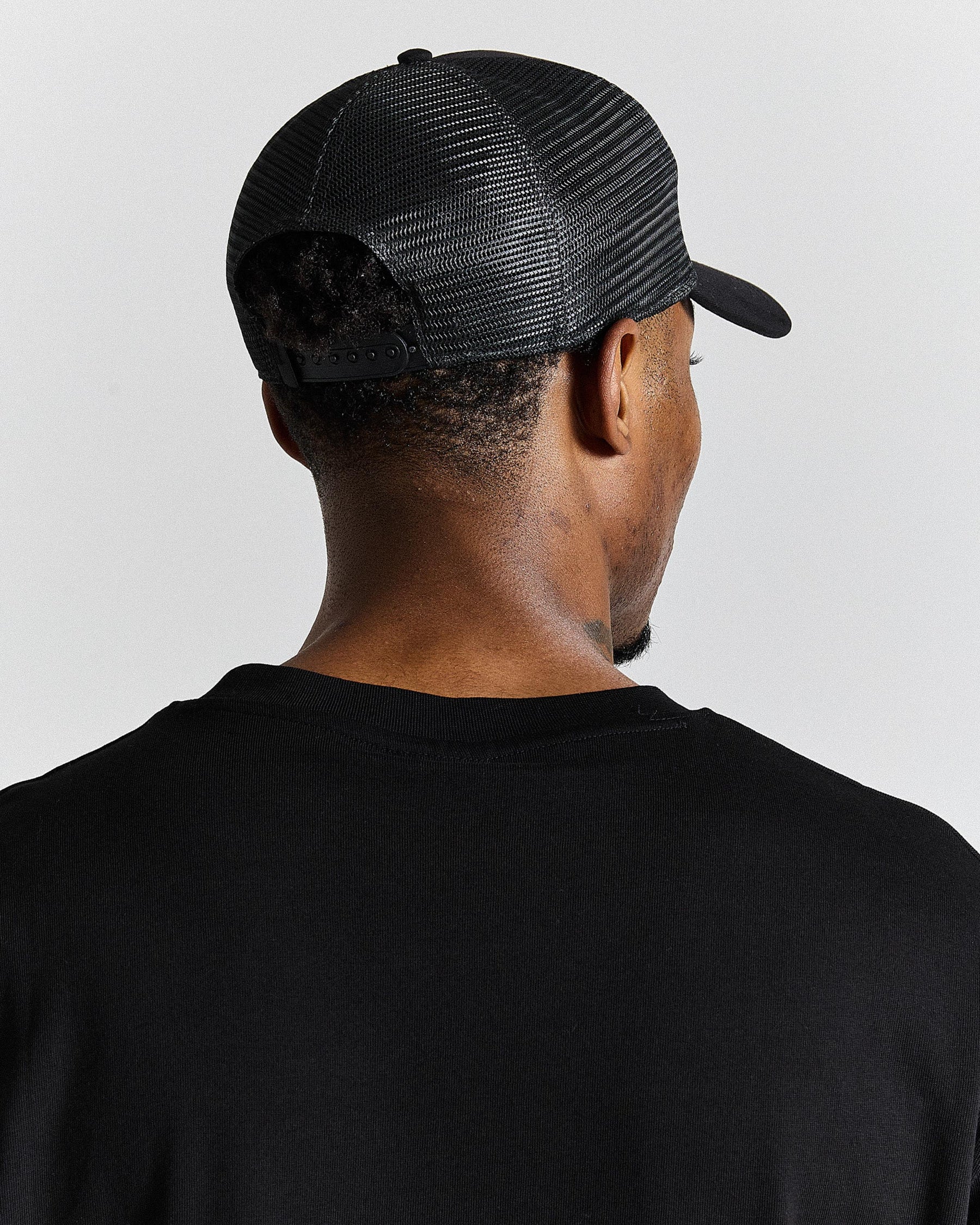 Person wearing a black mesh cap and black shirt on a light gray background