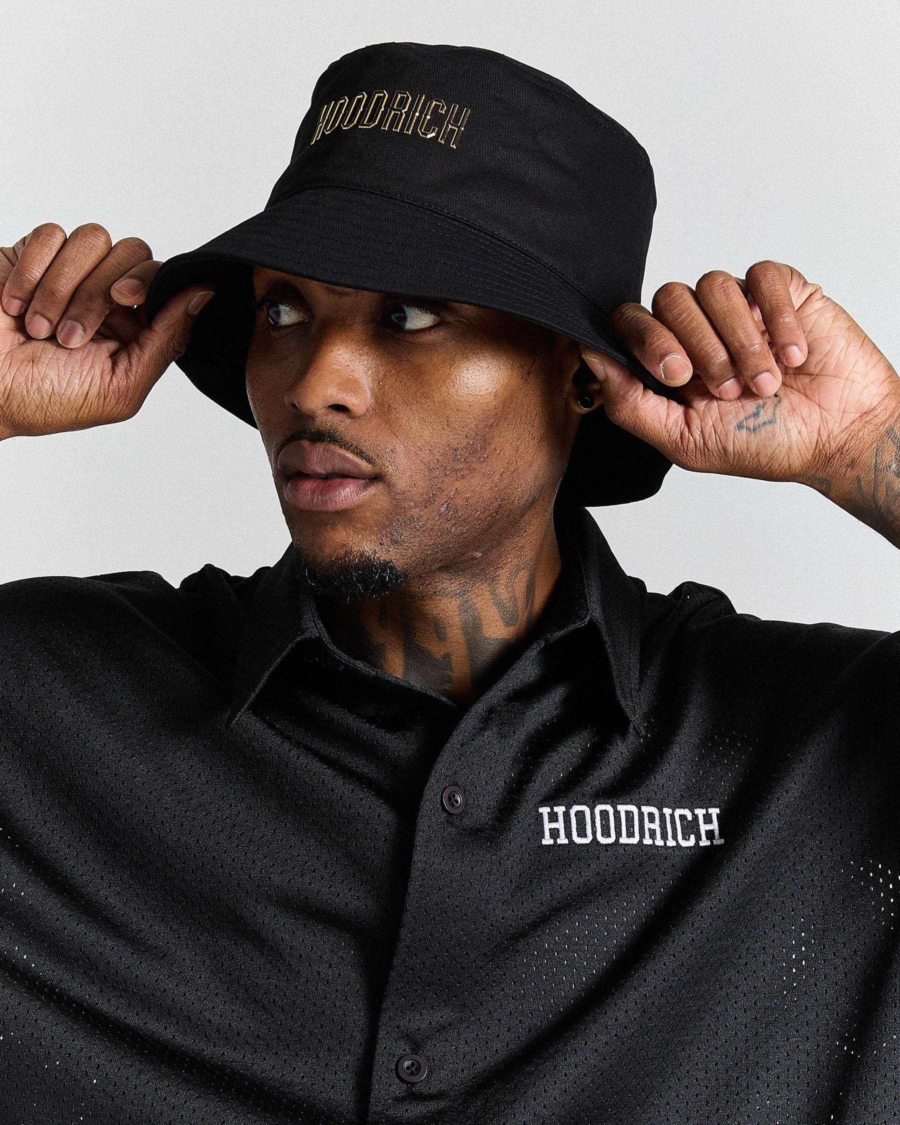 Man wearing a black 'Hoodrich' bucket hat and shirt against a light gray background